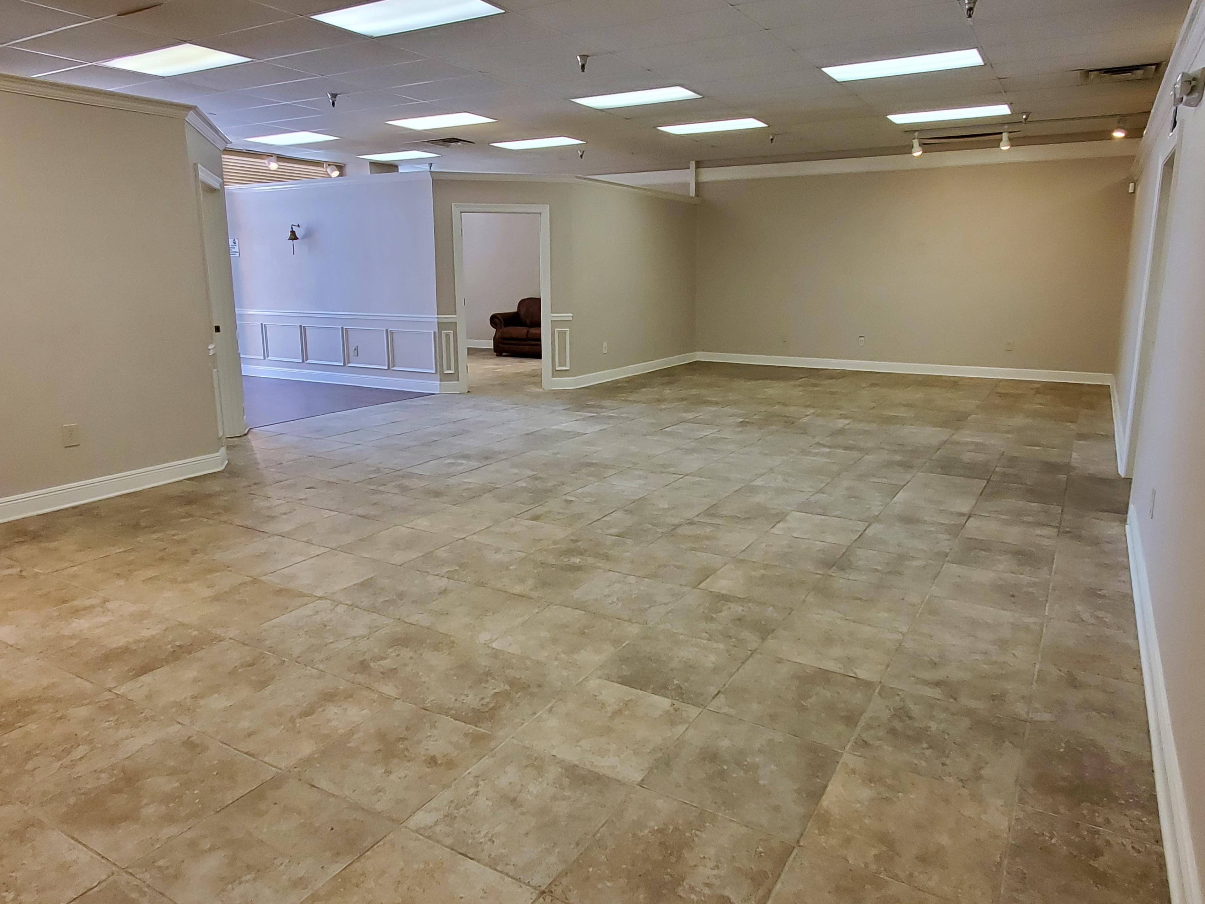 A spacious, empty room with tiled flooring, white walls, and several ceiling lights.