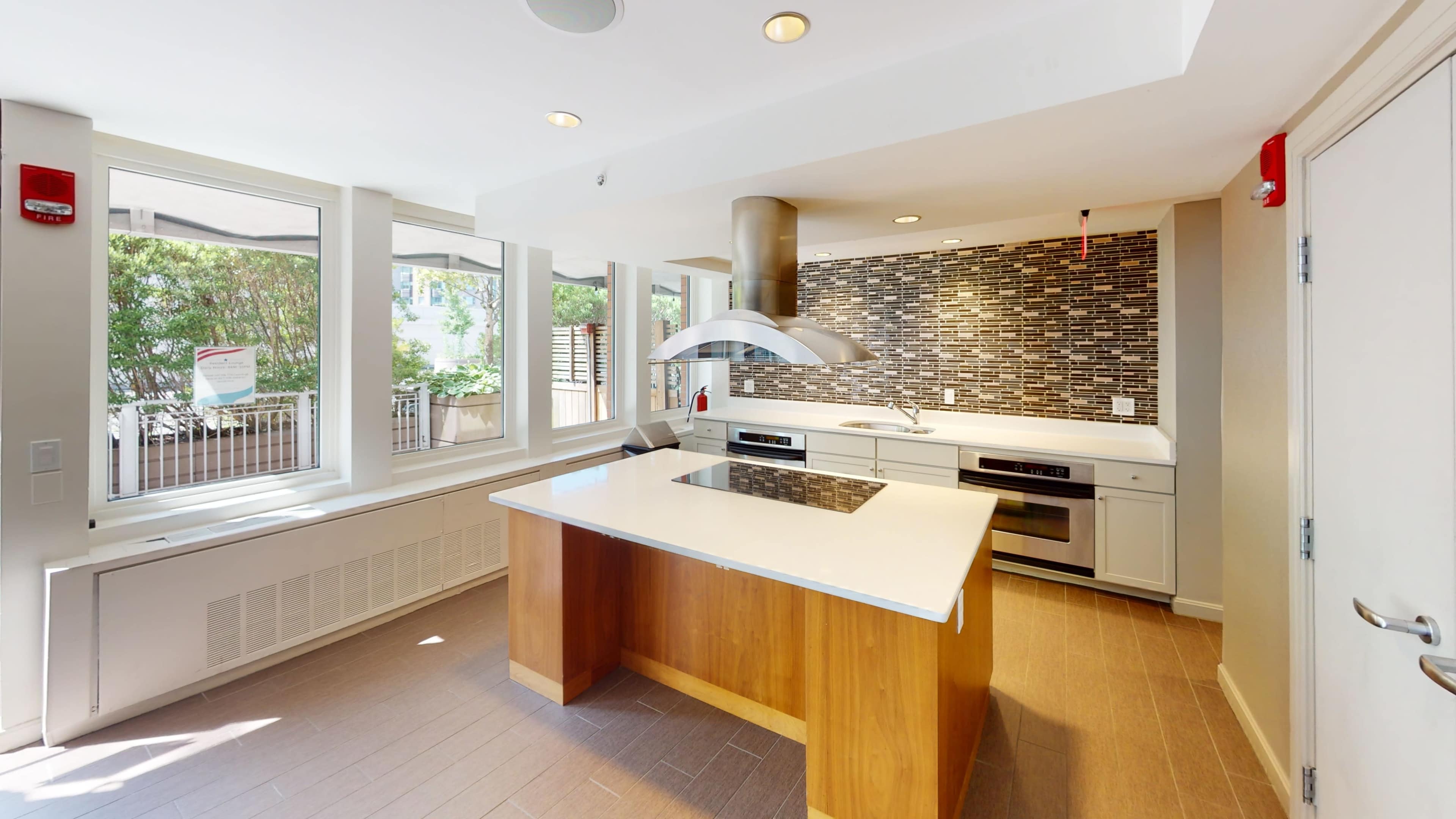 A modern kitchen with an island, a stainless steel range hood, and a mosaic backsplash.
