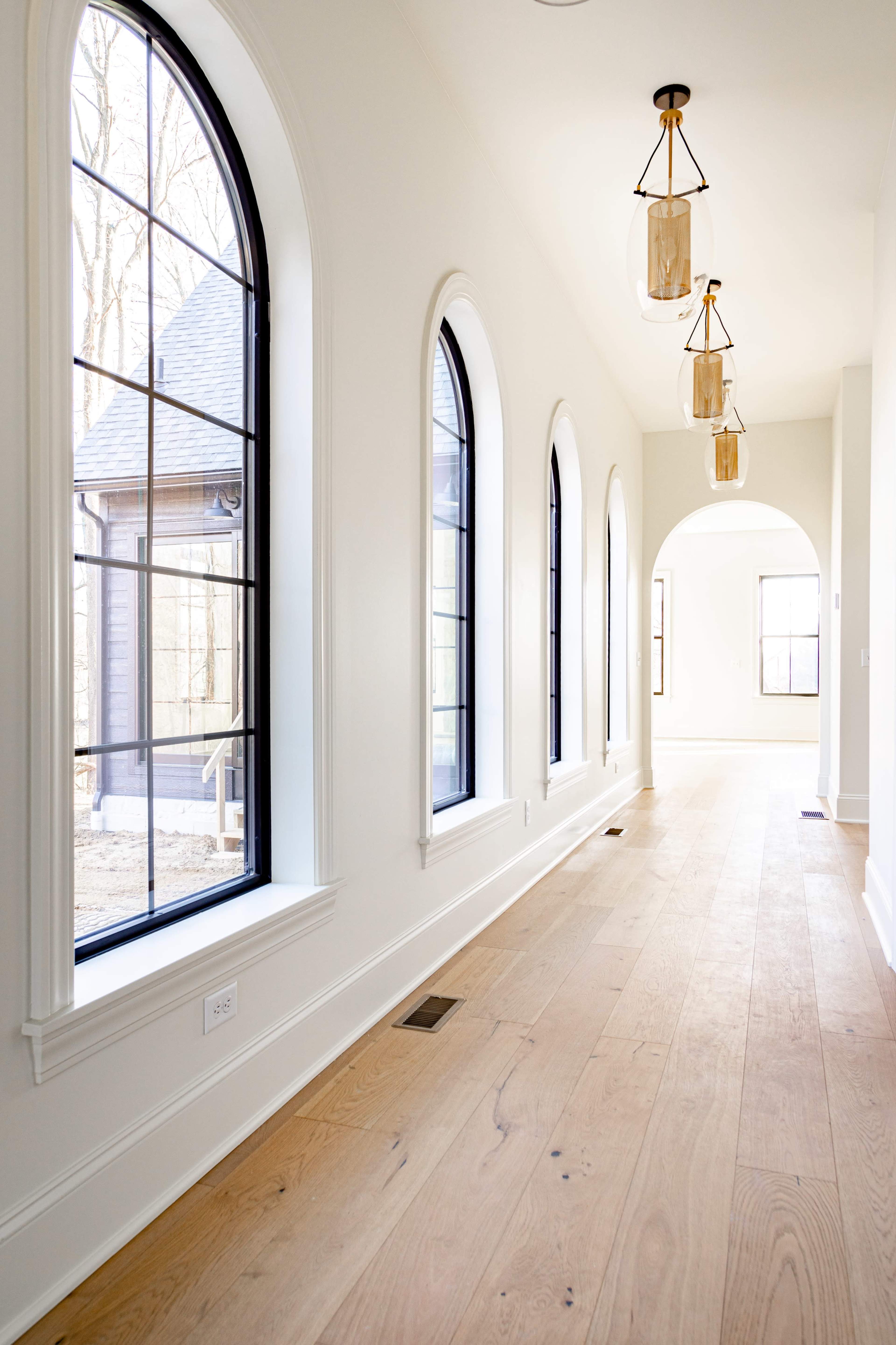 A well-lit hallway features arched windows on one side, with three pendant lights hanging from the ceiling.