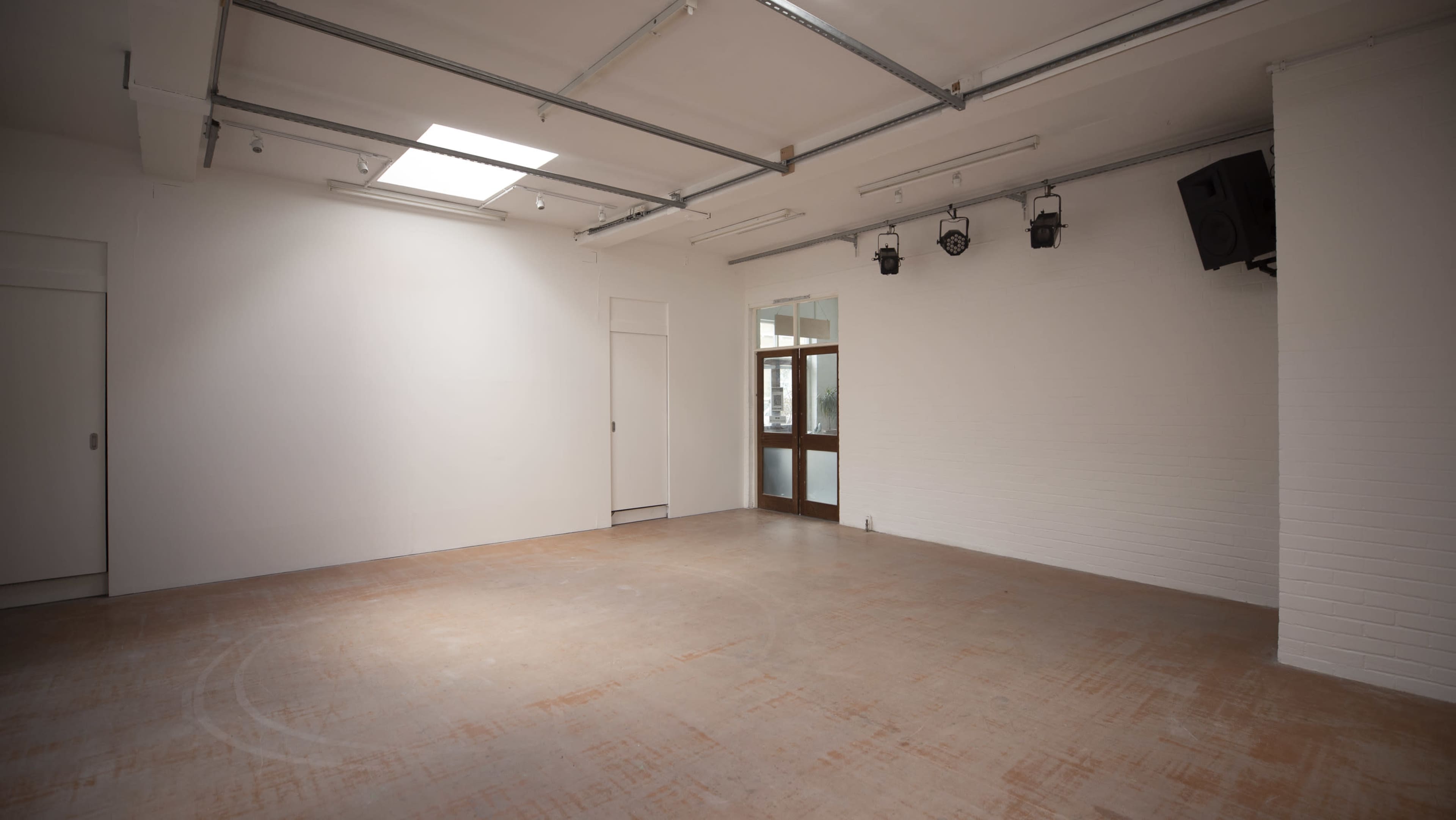 A spacious, empty room with white walls, a skylight, and a wooden door leading to an external area.