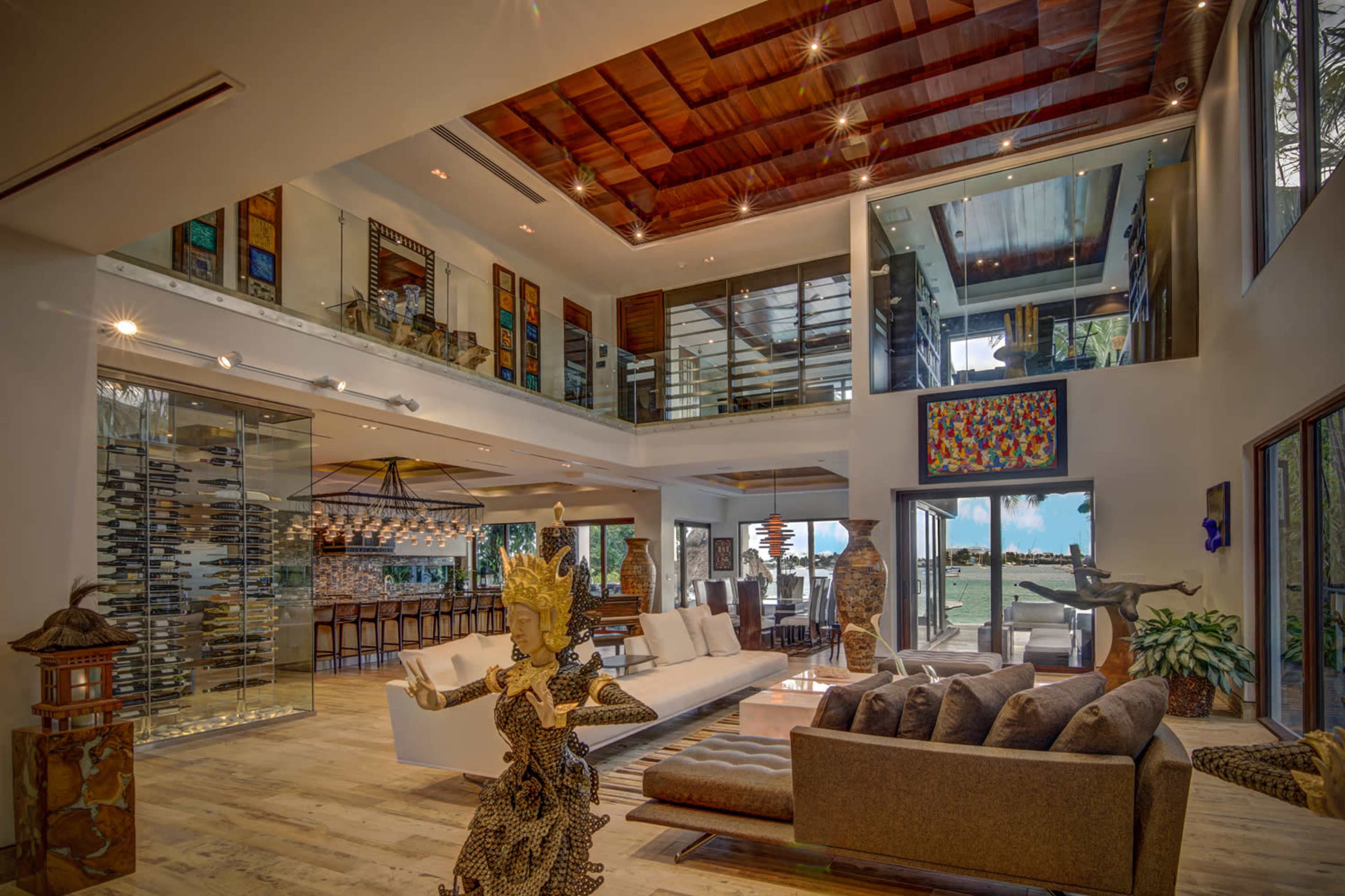 The interior of a modern home features a spacious living area with large windows, contemporary furniture, and decorative sculptures.