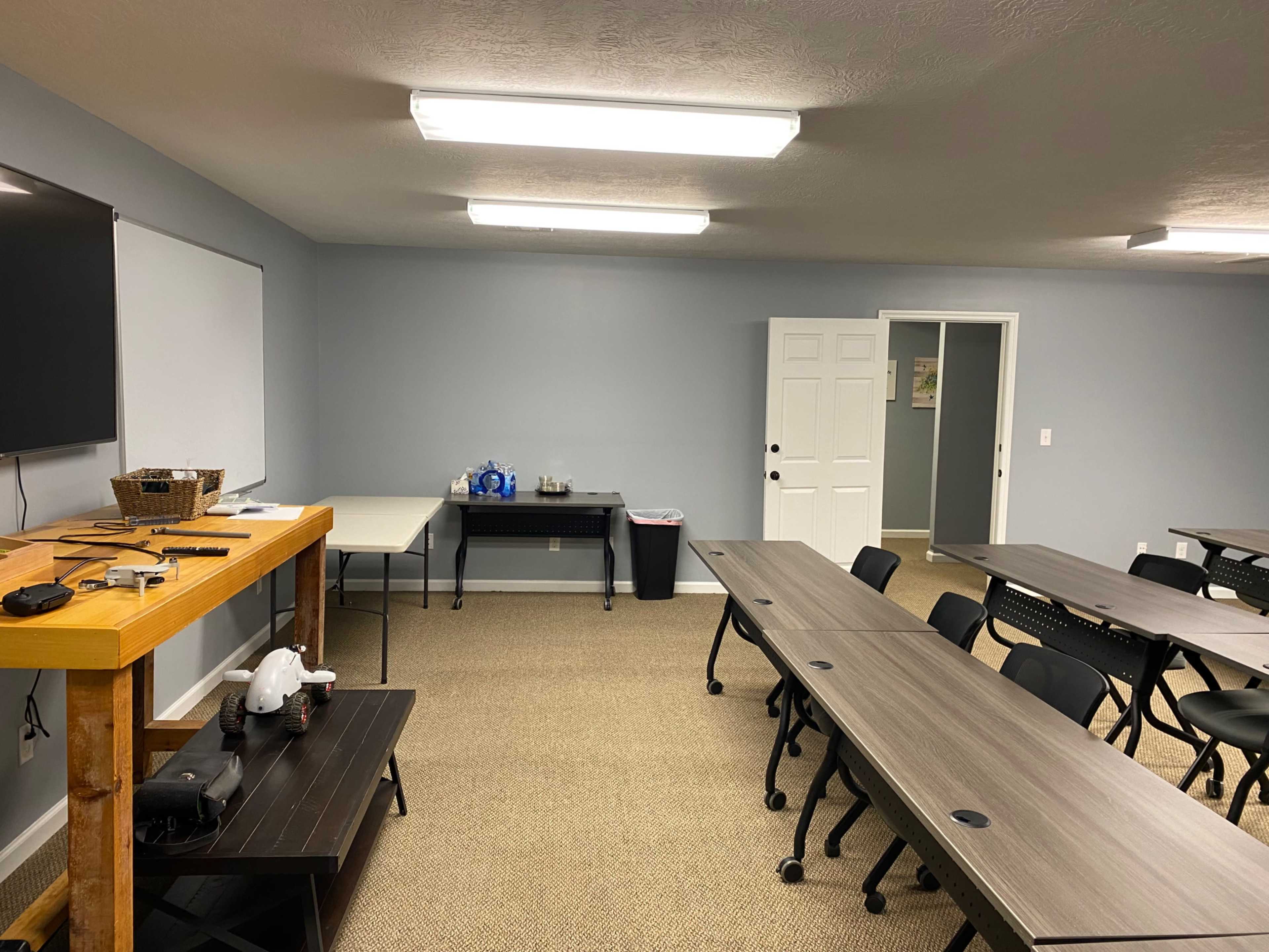 A meeting room with several tables and chairs arranged for a presentation, along with a wooden table and a whiteboard on one side.