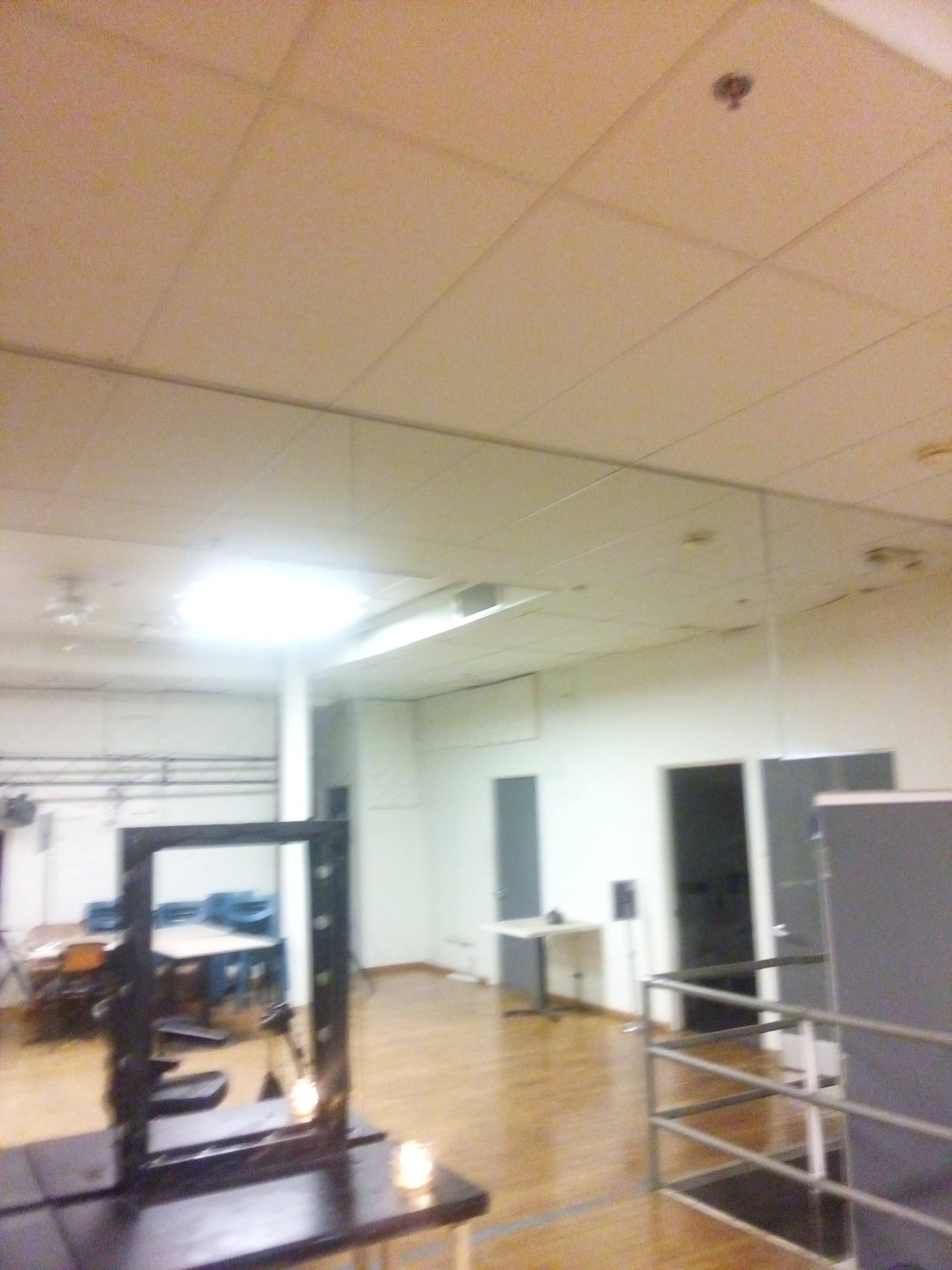 A spacious room with wooden flooring, white walls, and a large mirror on one side.