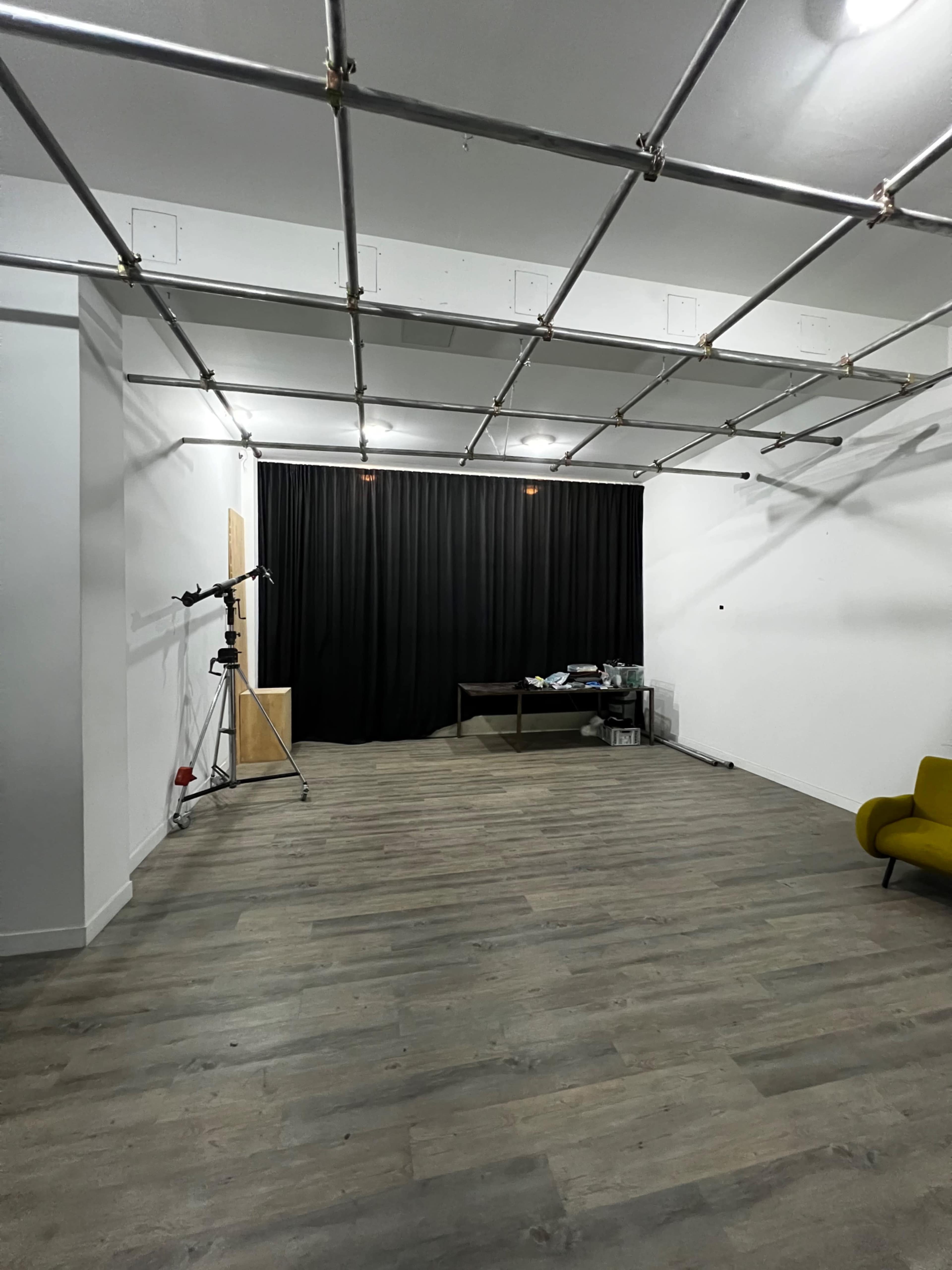 The image shows a spacious, empty studio with a black curtain at the back, a tripod, and a table against one wall.