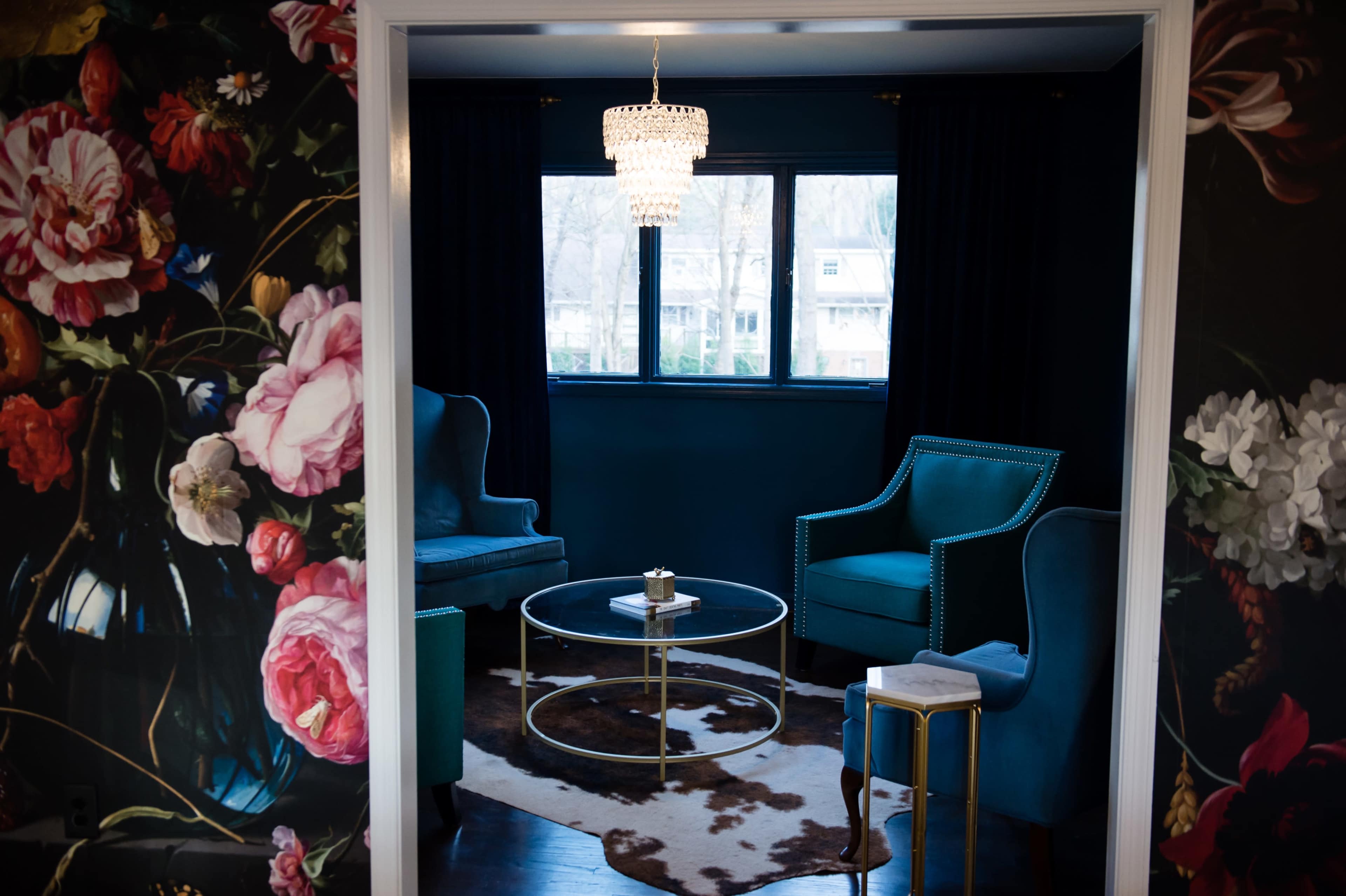 A cozy sitting area features turquoise armchairs and a glass coffee table, framed by floral wallpaper and a chandelier.