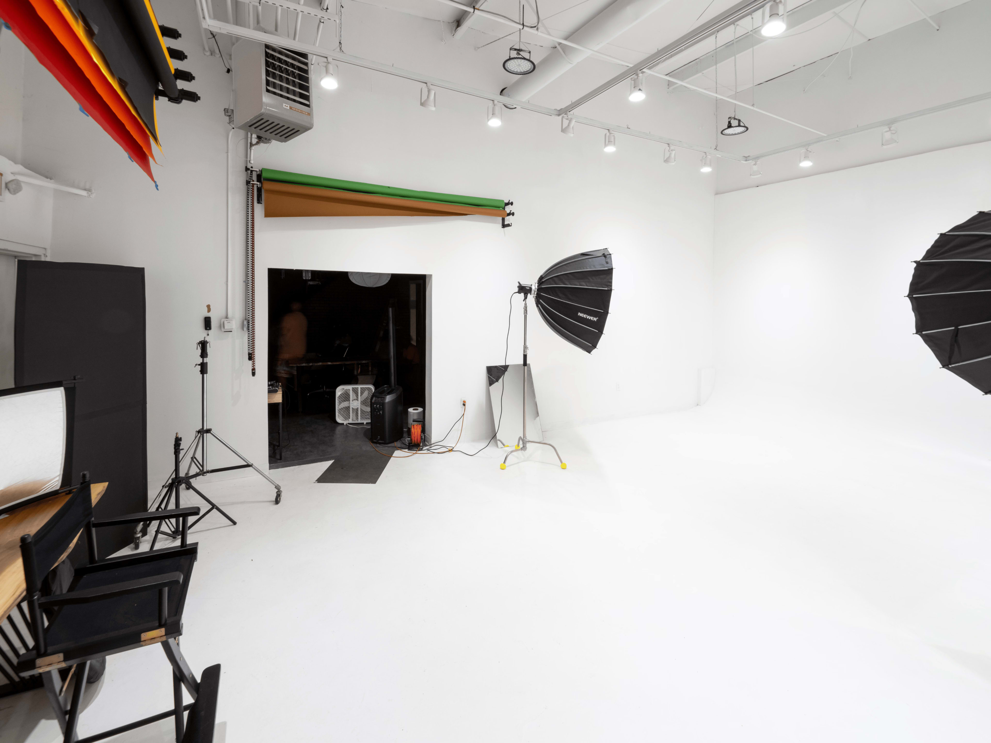 A photography studio with a white background, adjustable lighting equipment, and a few chairs arranged at a table.