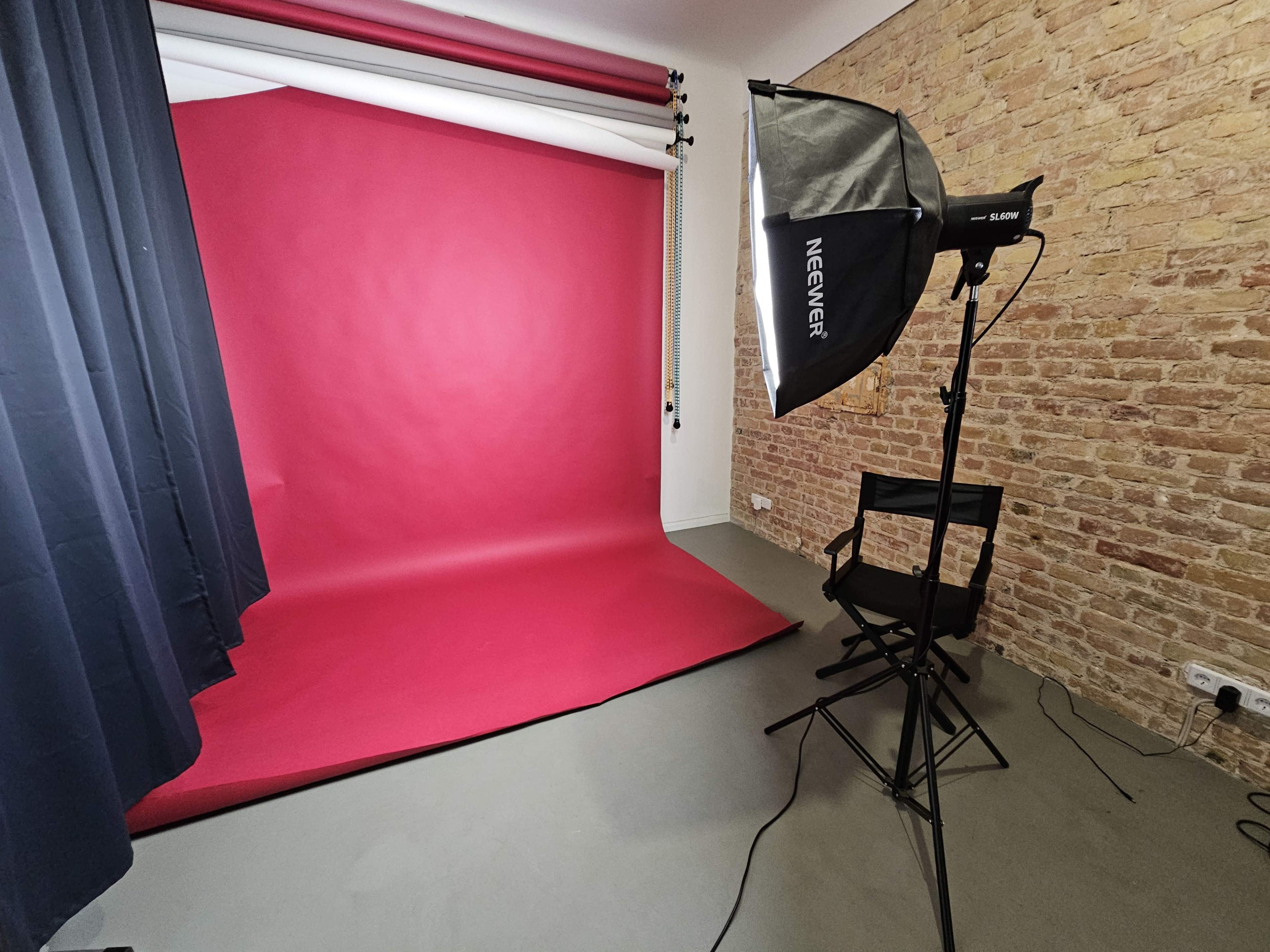 The image shows a photography studio setup with a red backdrop, a lighting umbrella on a stand, a black curtain, and an empty director's chair.