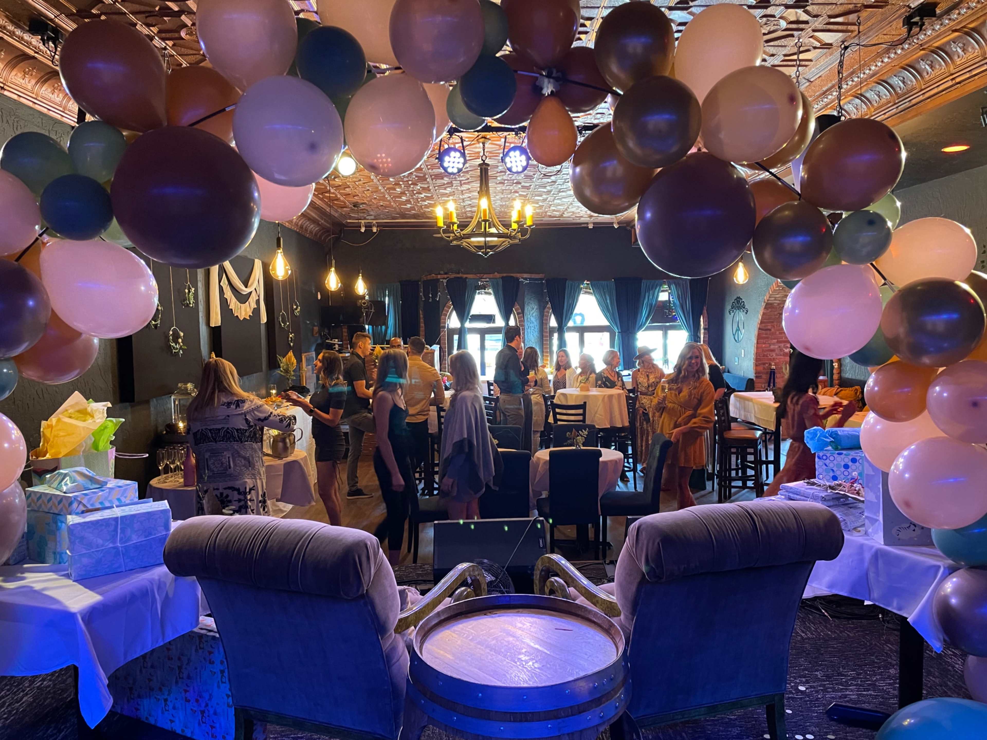 A festive indoor party setting with guests mingling under a decorative balloon arch.