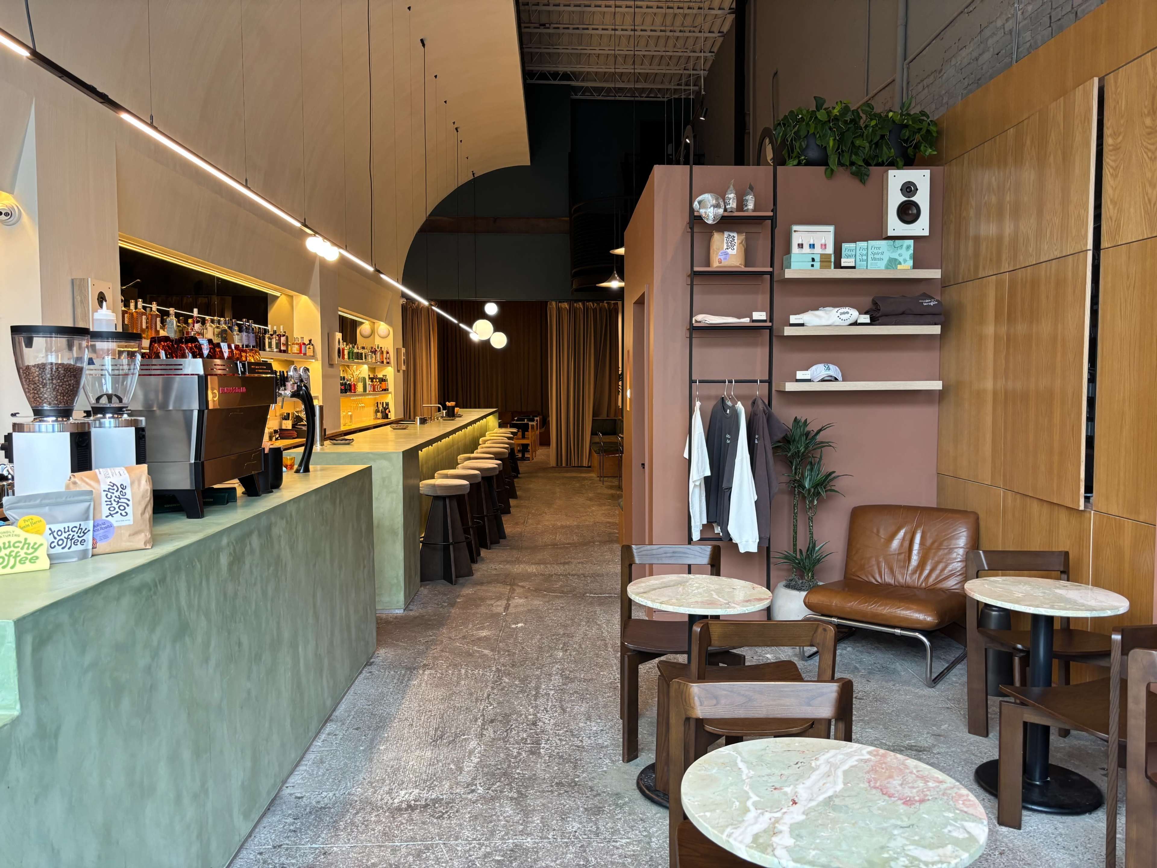 The image shows a modern café interior featuring a long green counter with seating, wooden furniture, and shelves displaying various items.