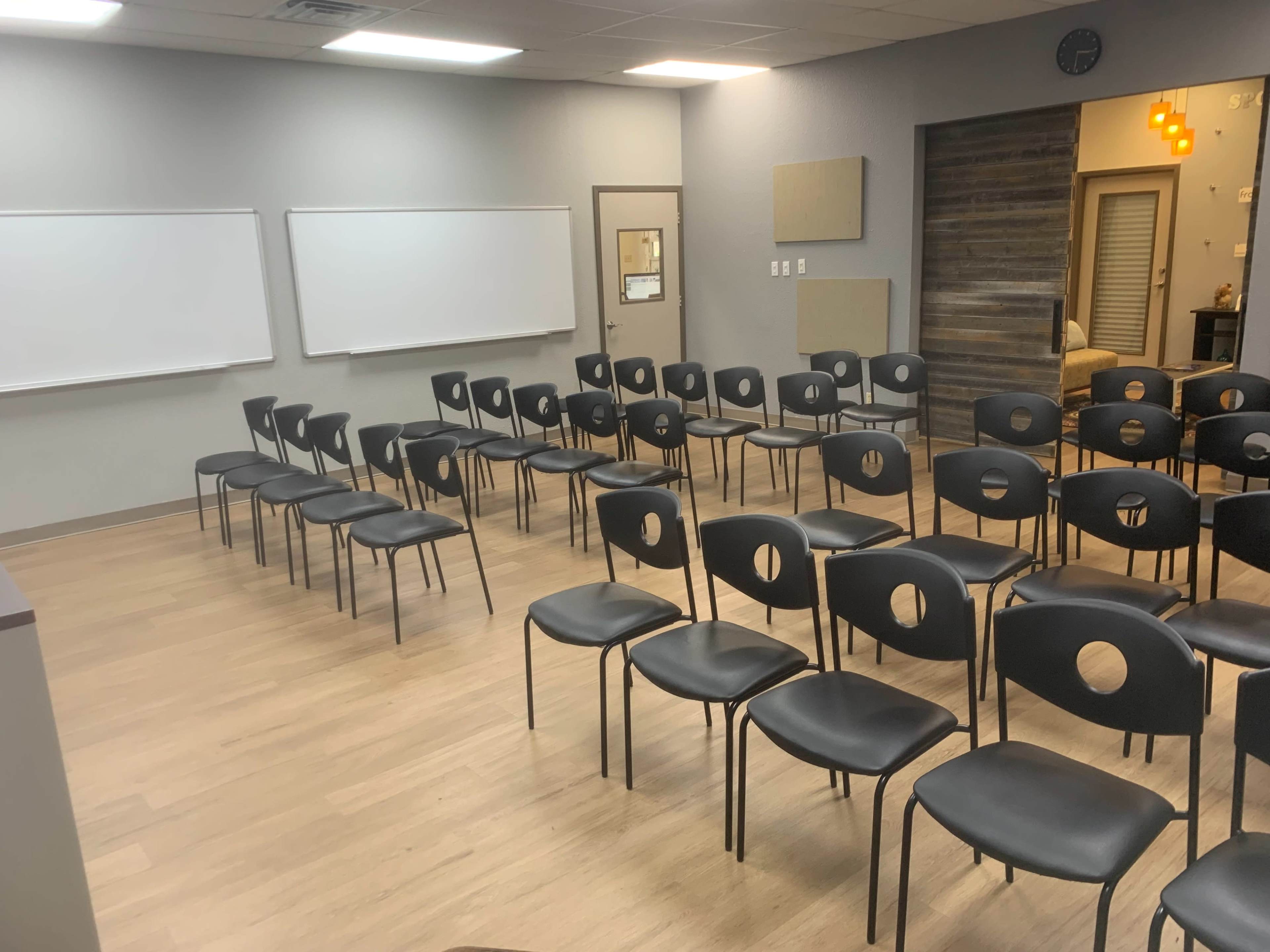 The image shows a classroom setup with several rows of black chairs arranged in front of whiteboards.