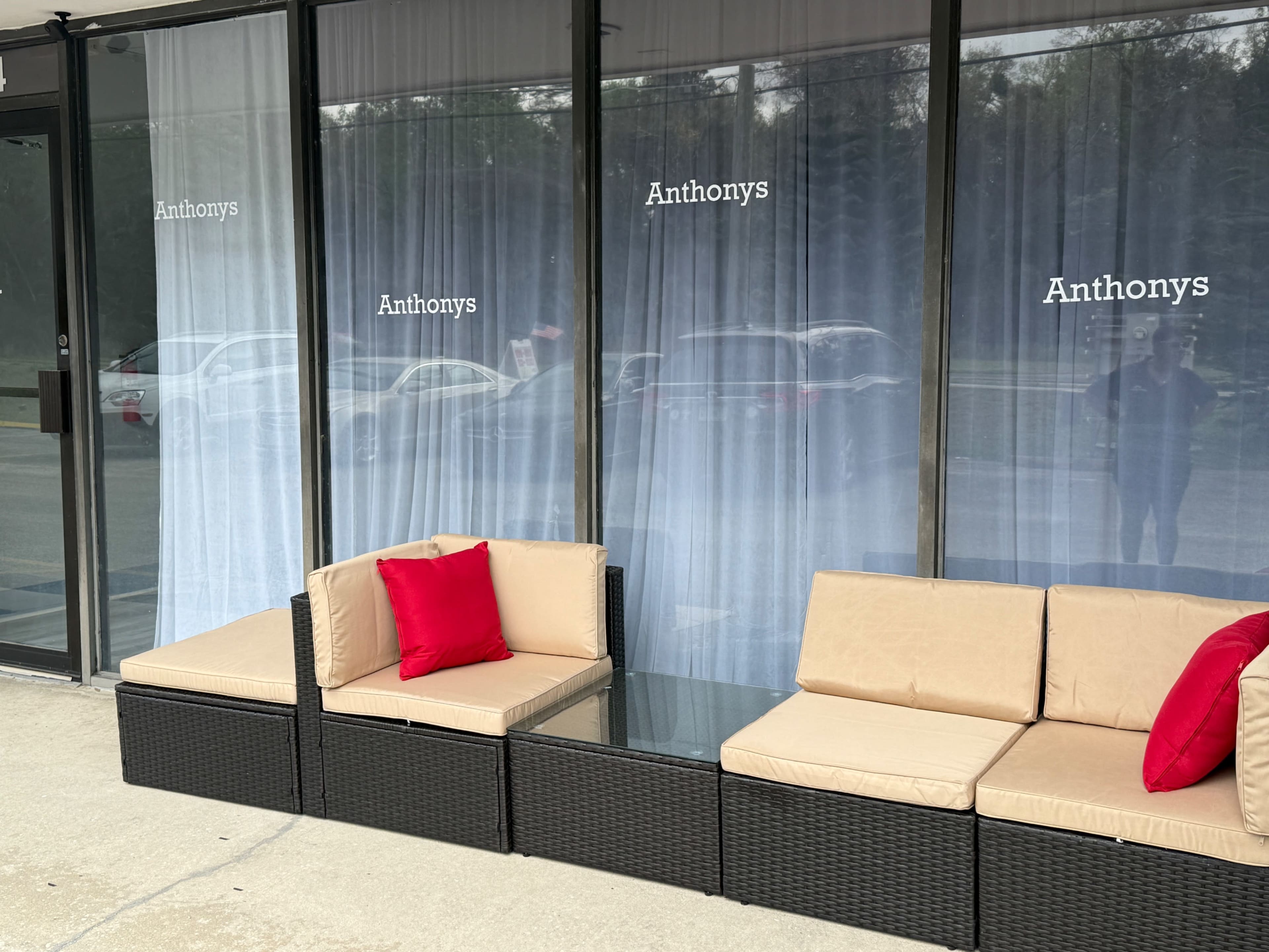 The image shows a seating area with beige cushions and red accent pillows in front of a glass storefront featuring the name "Anthonys" on the windows.