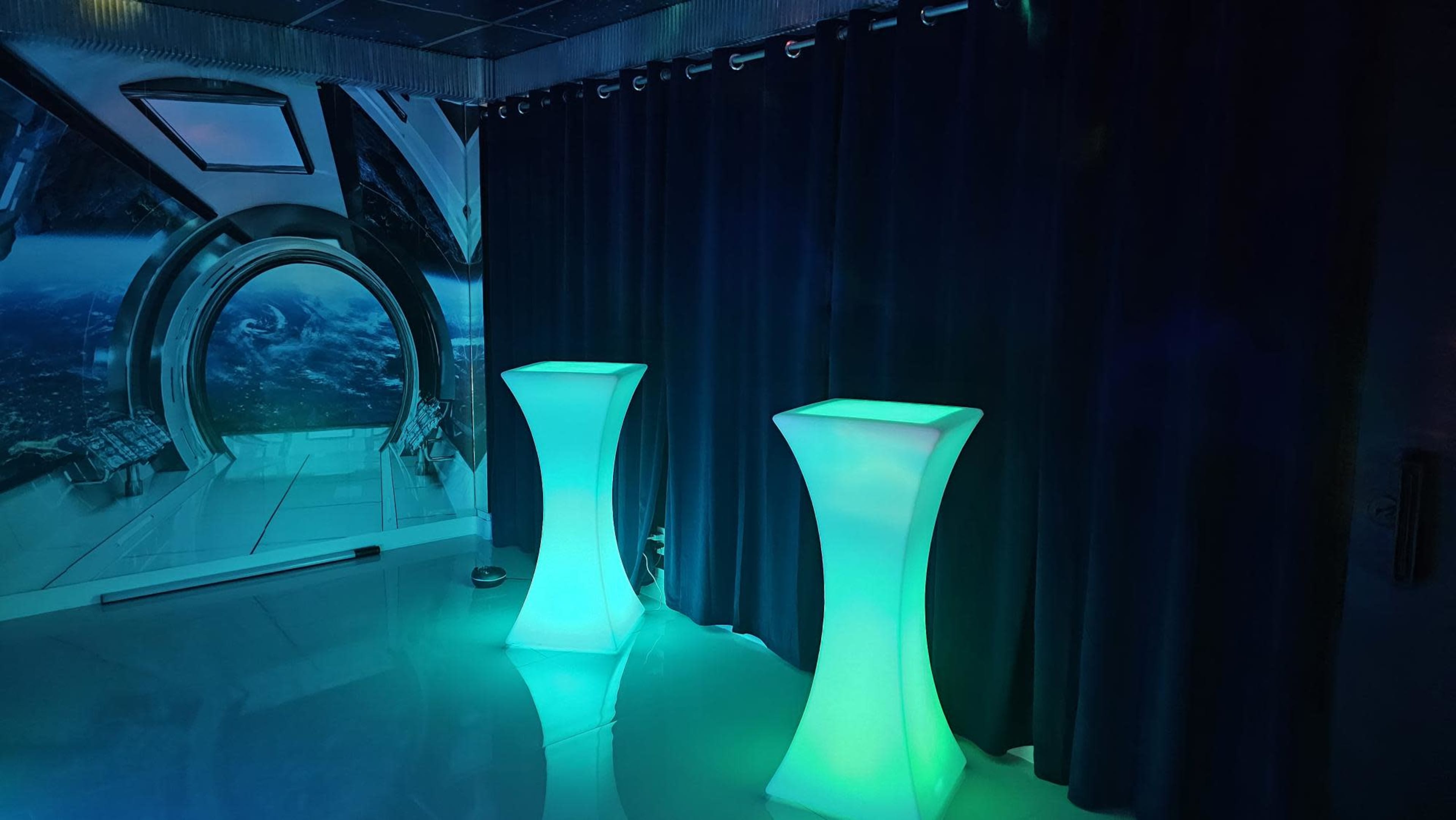 A futuristic room with two illuminated podiums against a backdrop of dark curtains and a space-themed wall mural.
