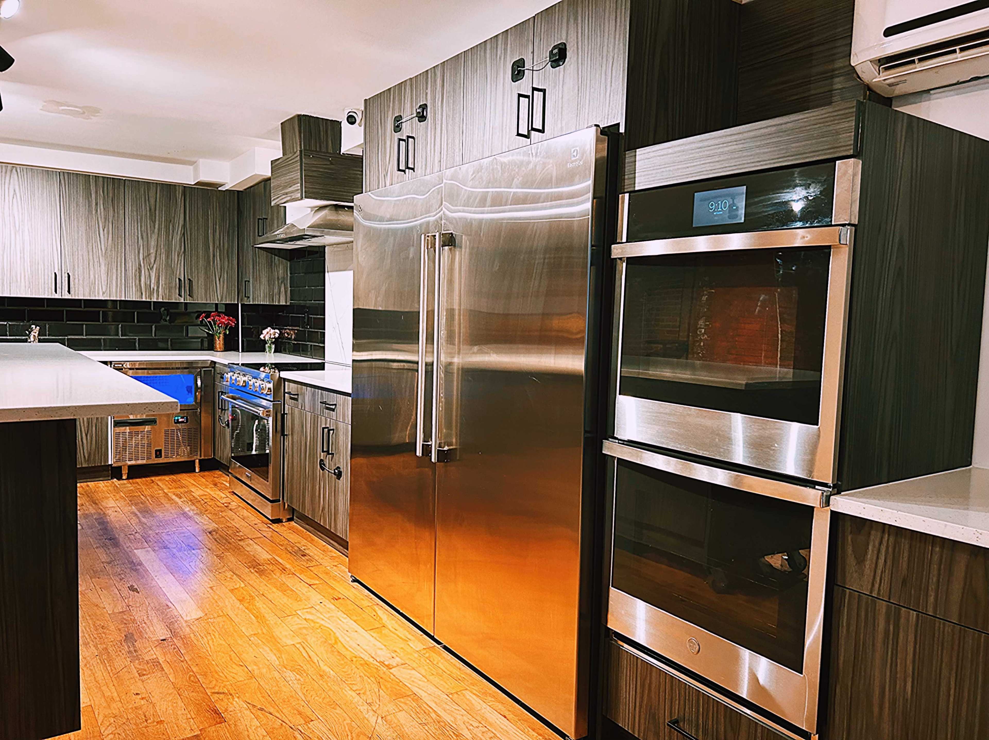 A modern kitchen features stainless steel appliances, including a refrigerator and double ovens, with wooden cabinetry and a large island.