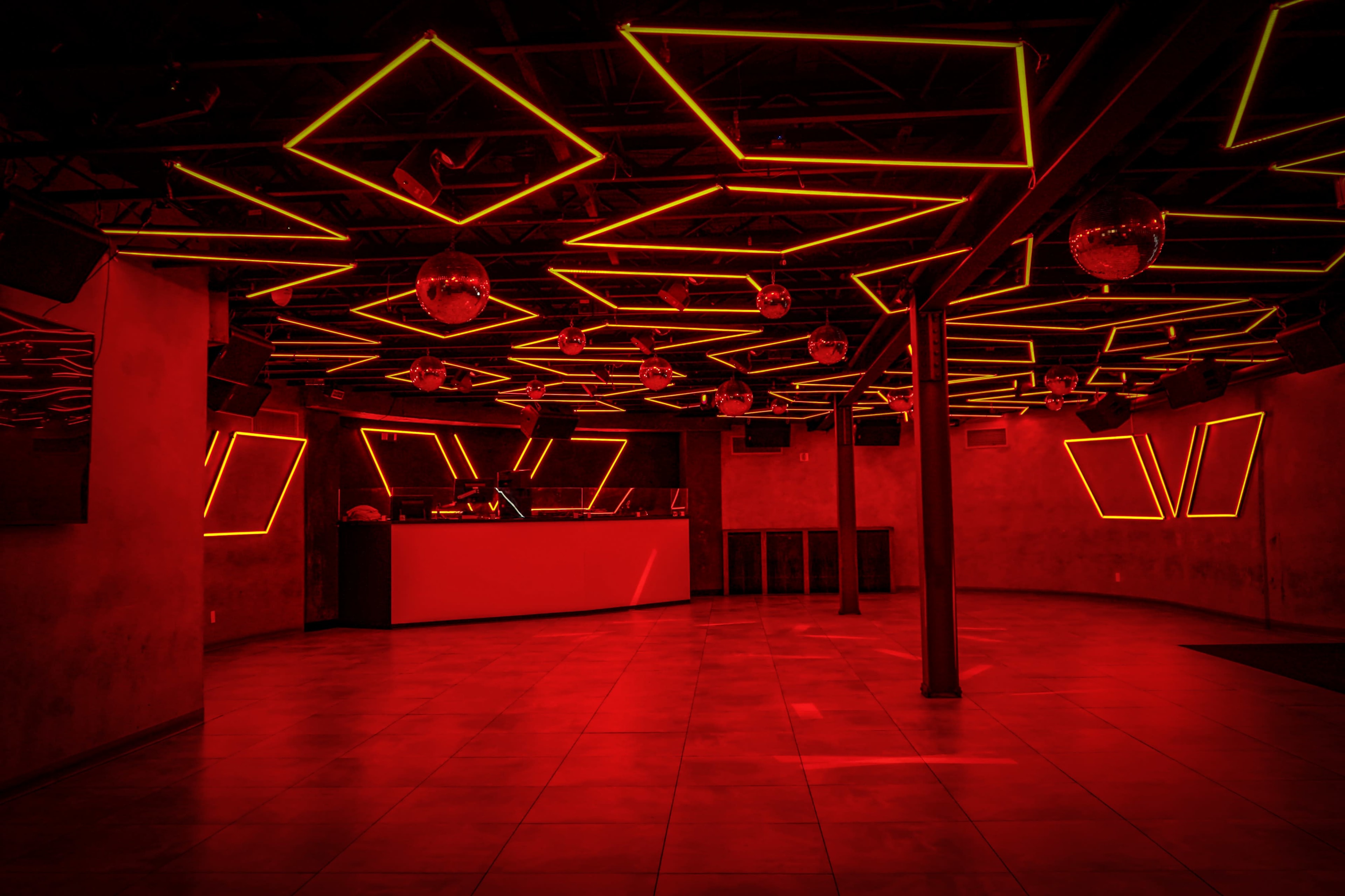 The image shows a dimly lit nightclub interior with red neon lights and a bar area in the background.