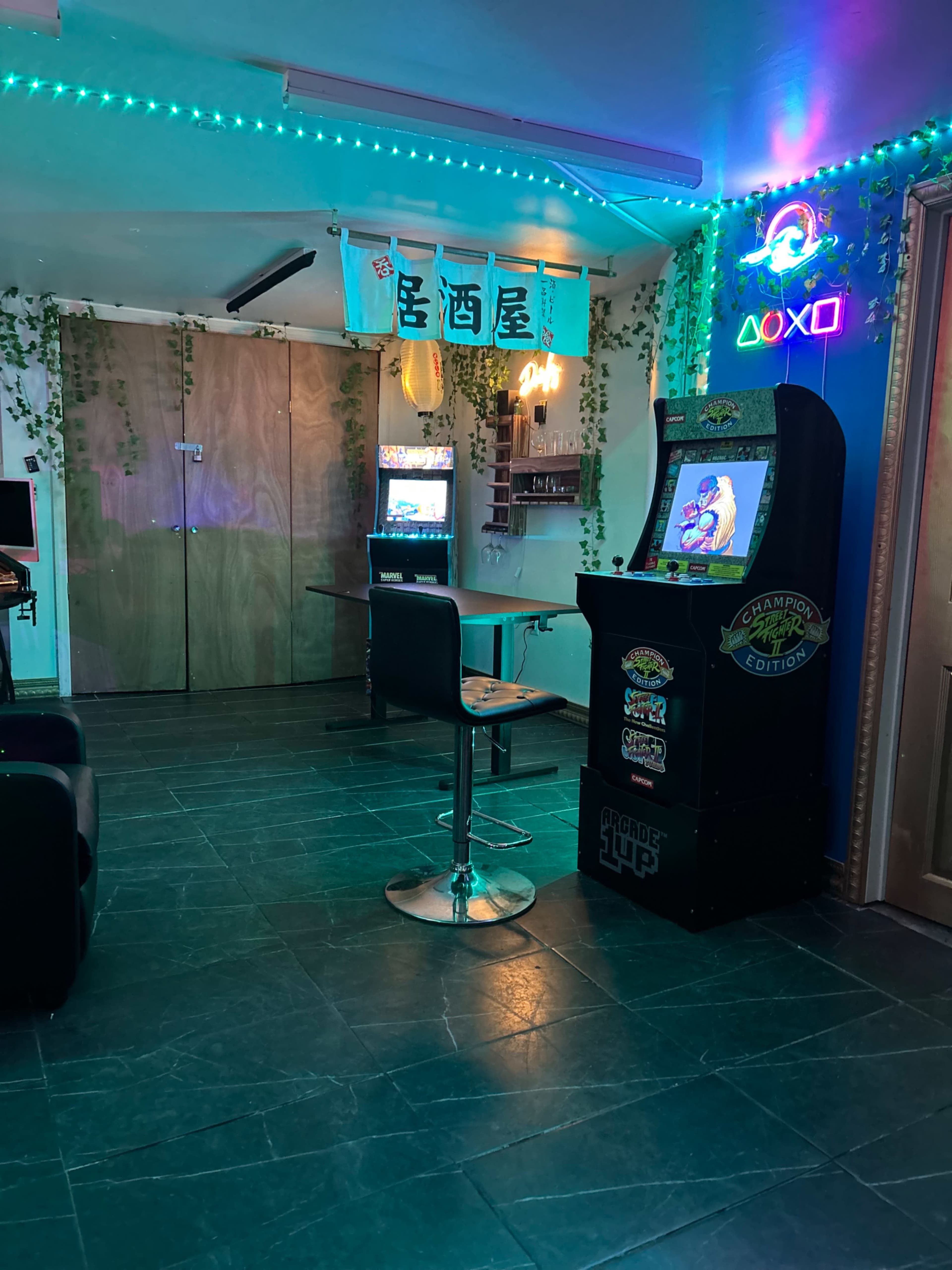 The scene features a retro arcade setup with a video game cabinet, a bar-style seating area, and neon lights amidst green decorative plants.