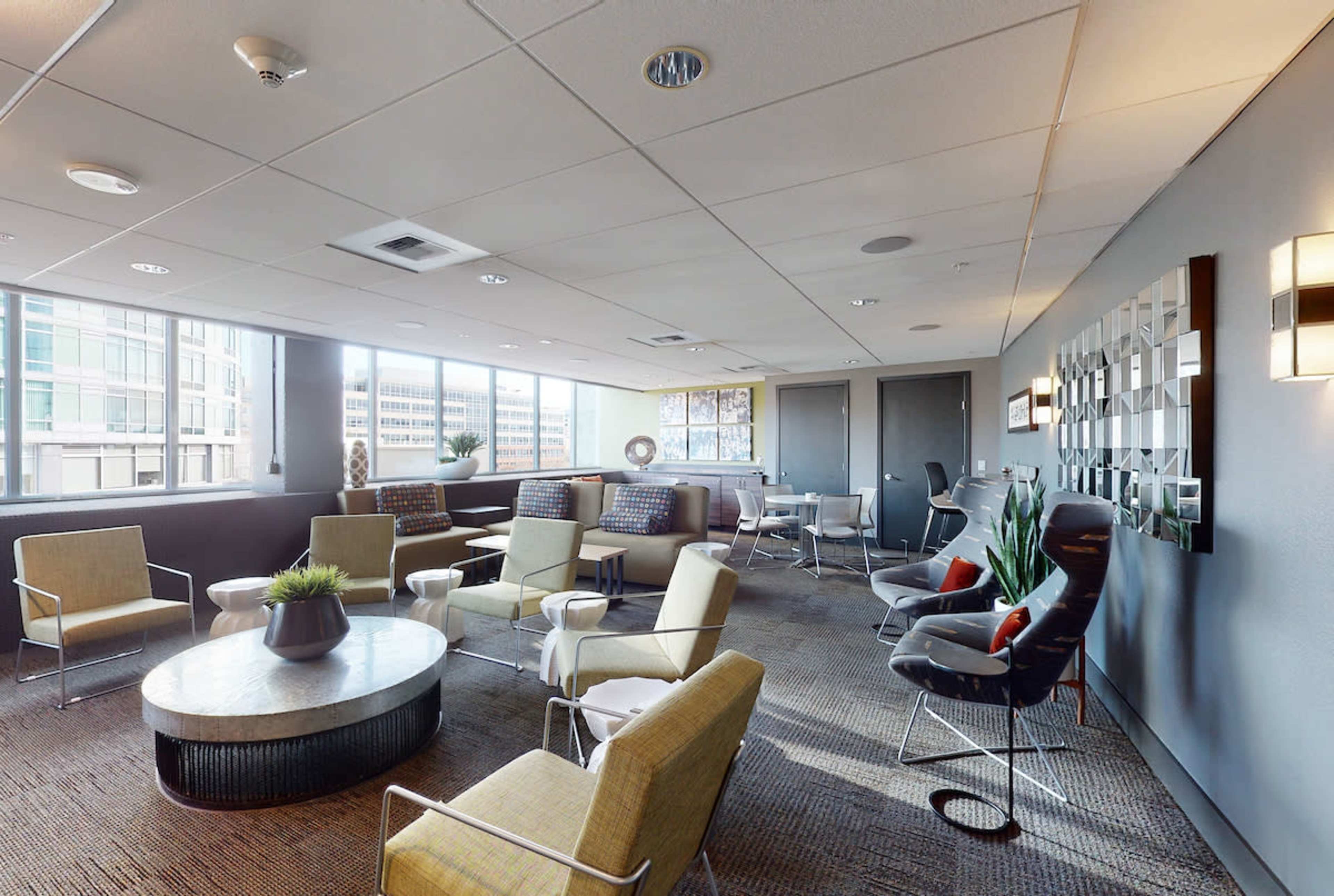 A modern lounge area features comfortable seating, large windows, and a small dining table.