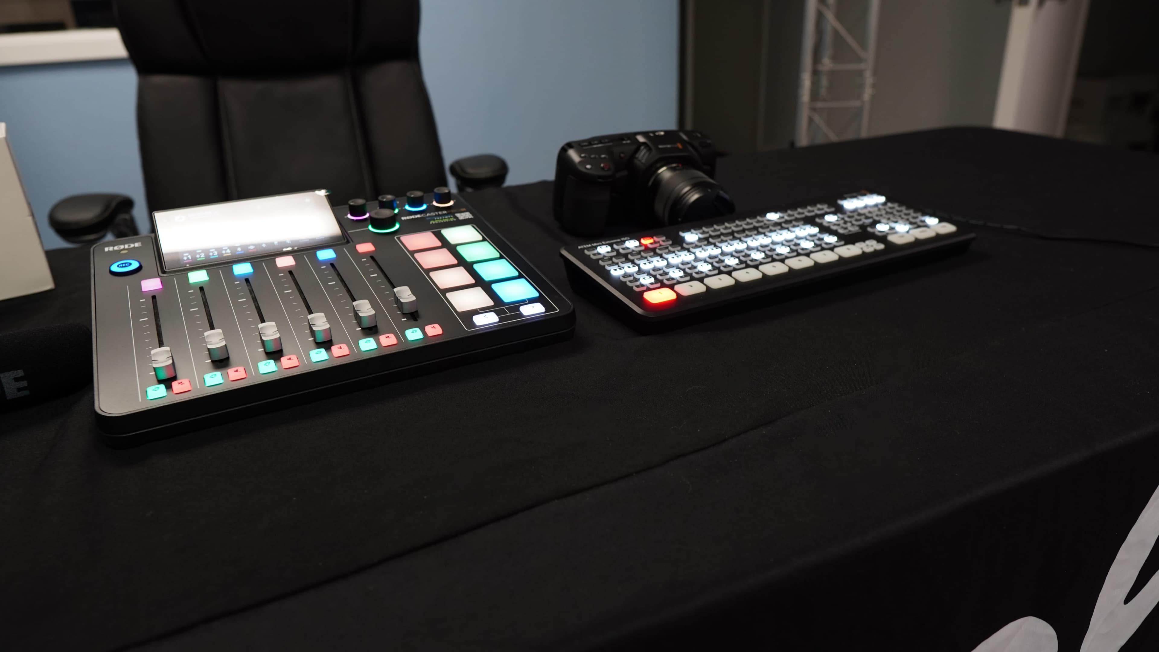 A video production setup featuring a control surface with buttons and sliders alongside a camera on a black tablecloth.