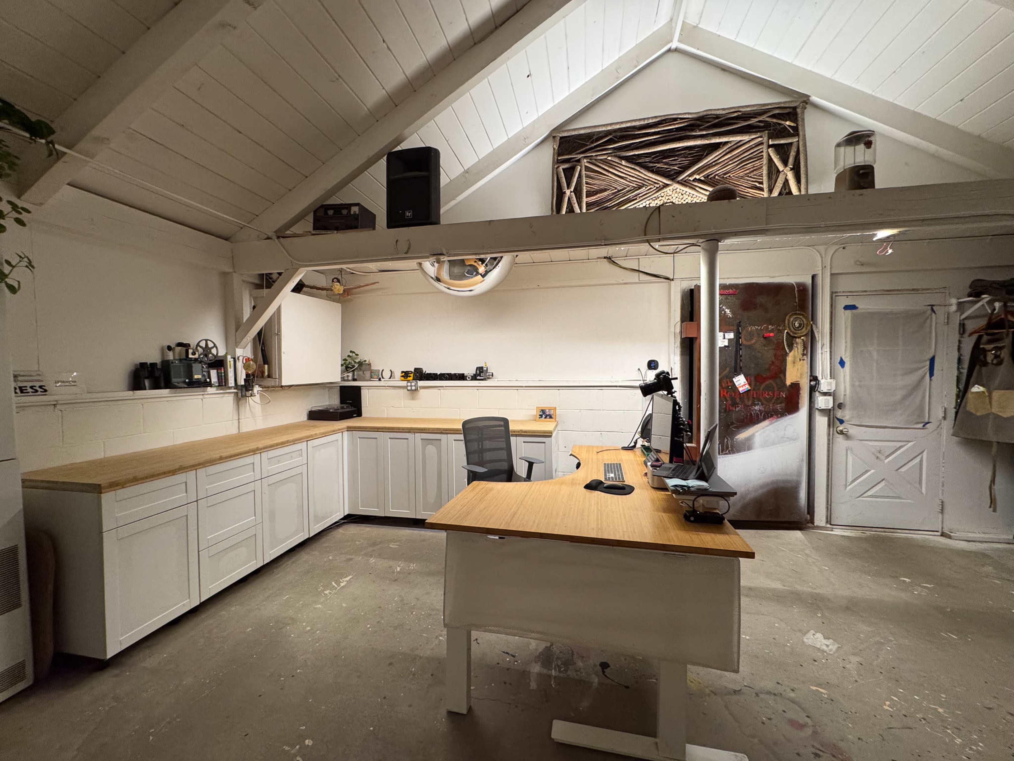 The image shows a workspace with a wooden desk and a large counter, illuminated by natural light from the open door and windows.