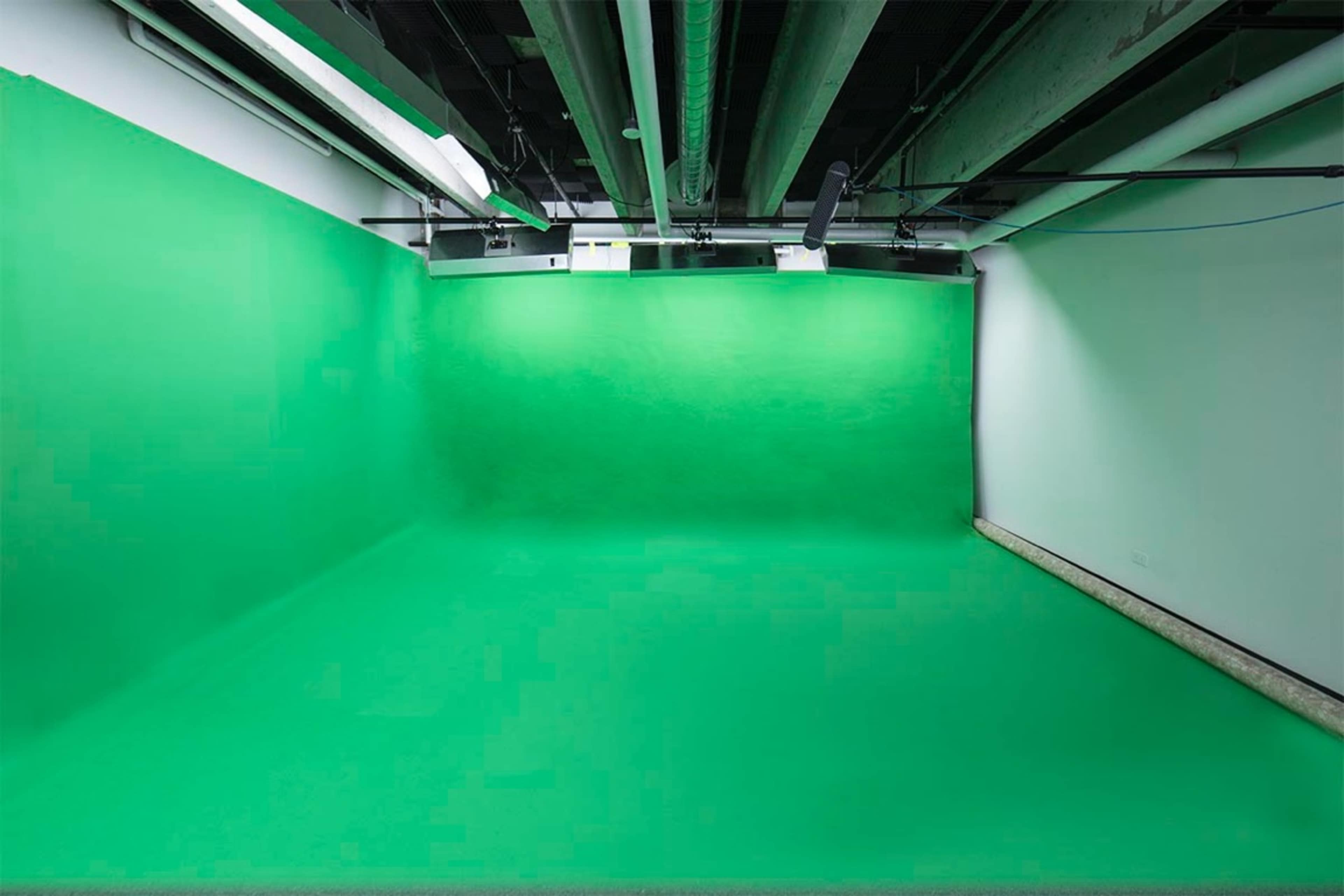 A spacious room with a green backdrop and flooring, commonly used for video production or photography.