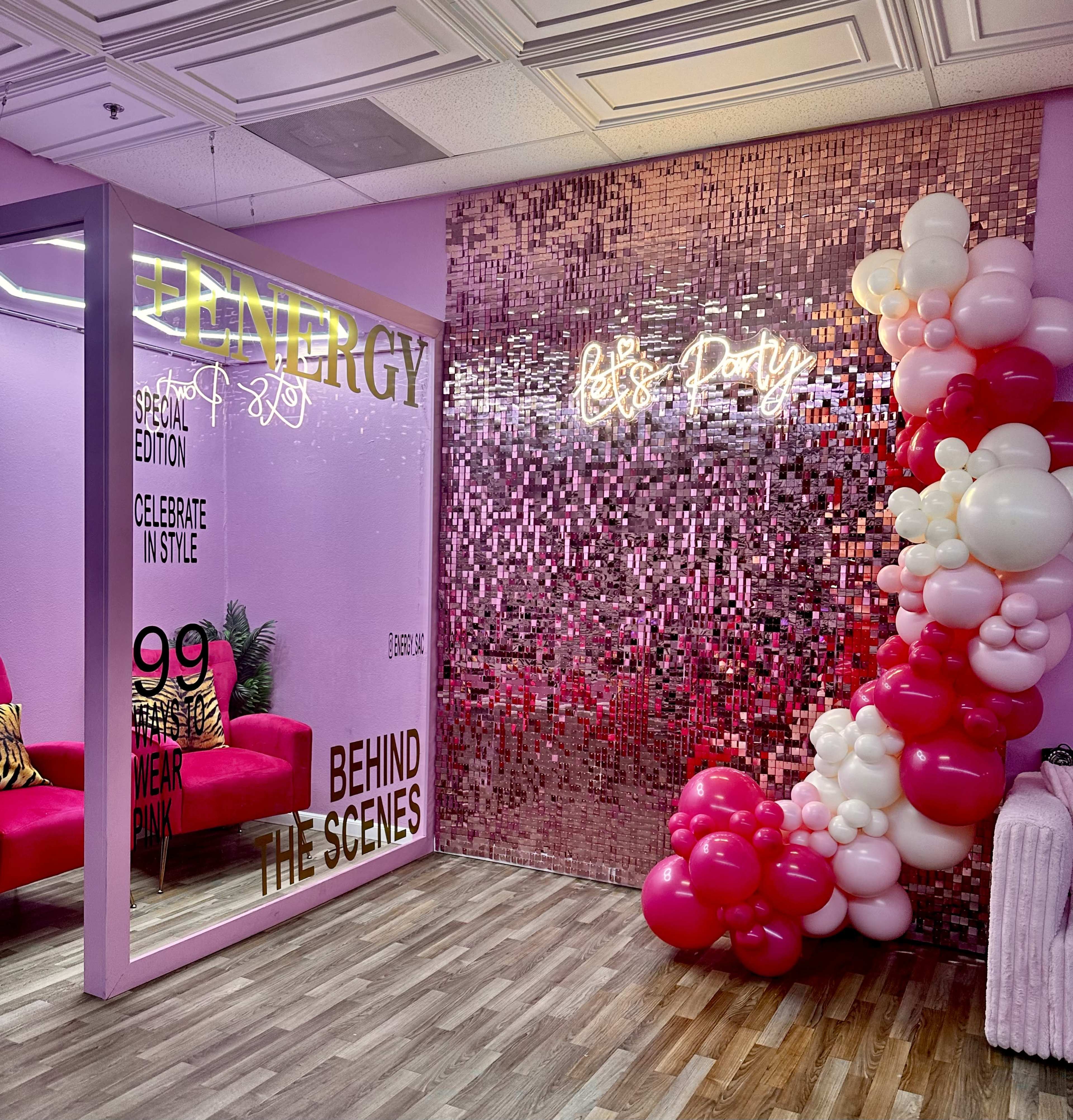 The image shows a vibrant pink-themed party room with a glittering wall, decorative balloons, and a neon sign that reads "Let's Party."