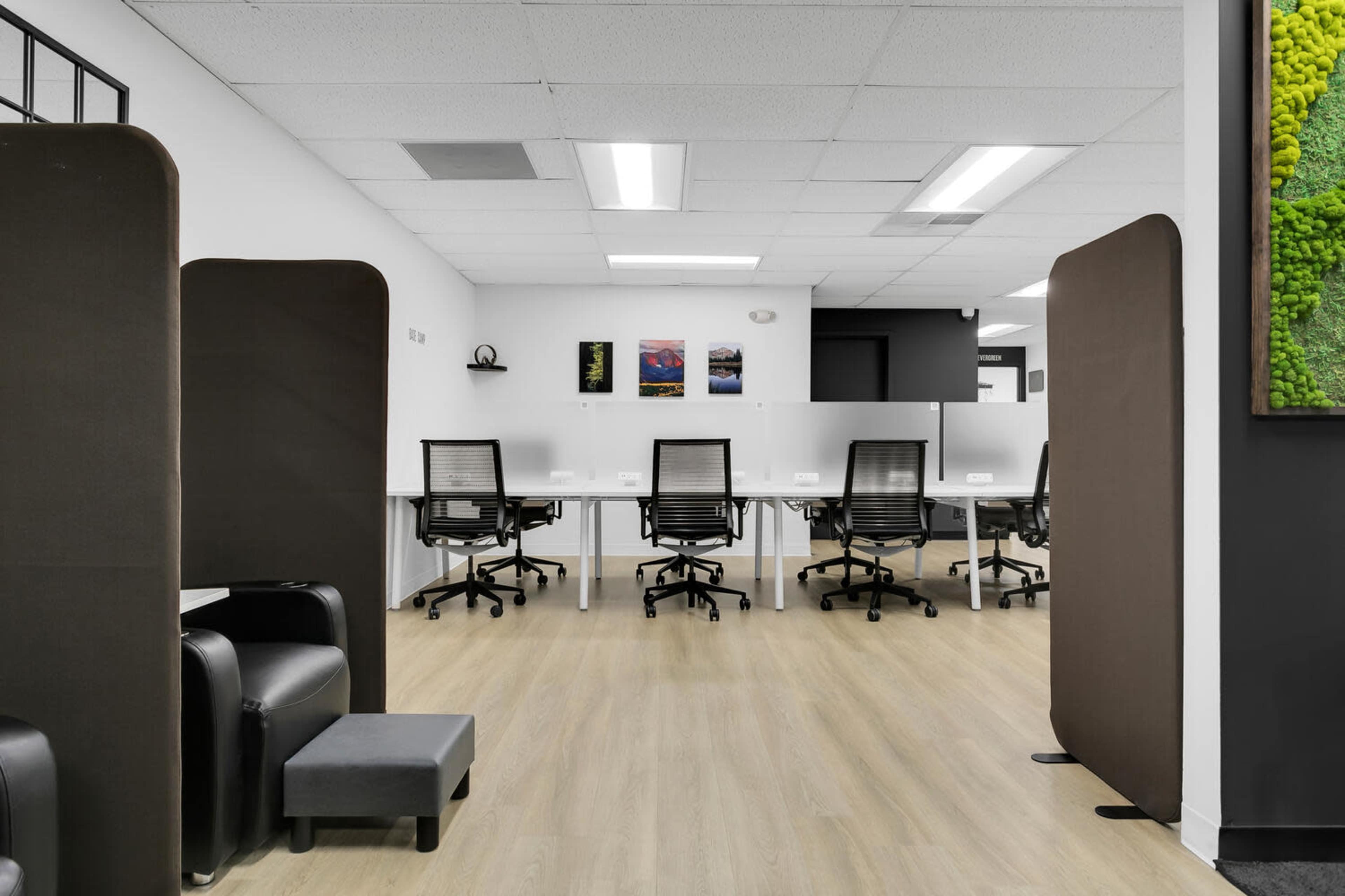 The image shows a modern office space with several desks, ergonomic chairs, and partitions for privacy.