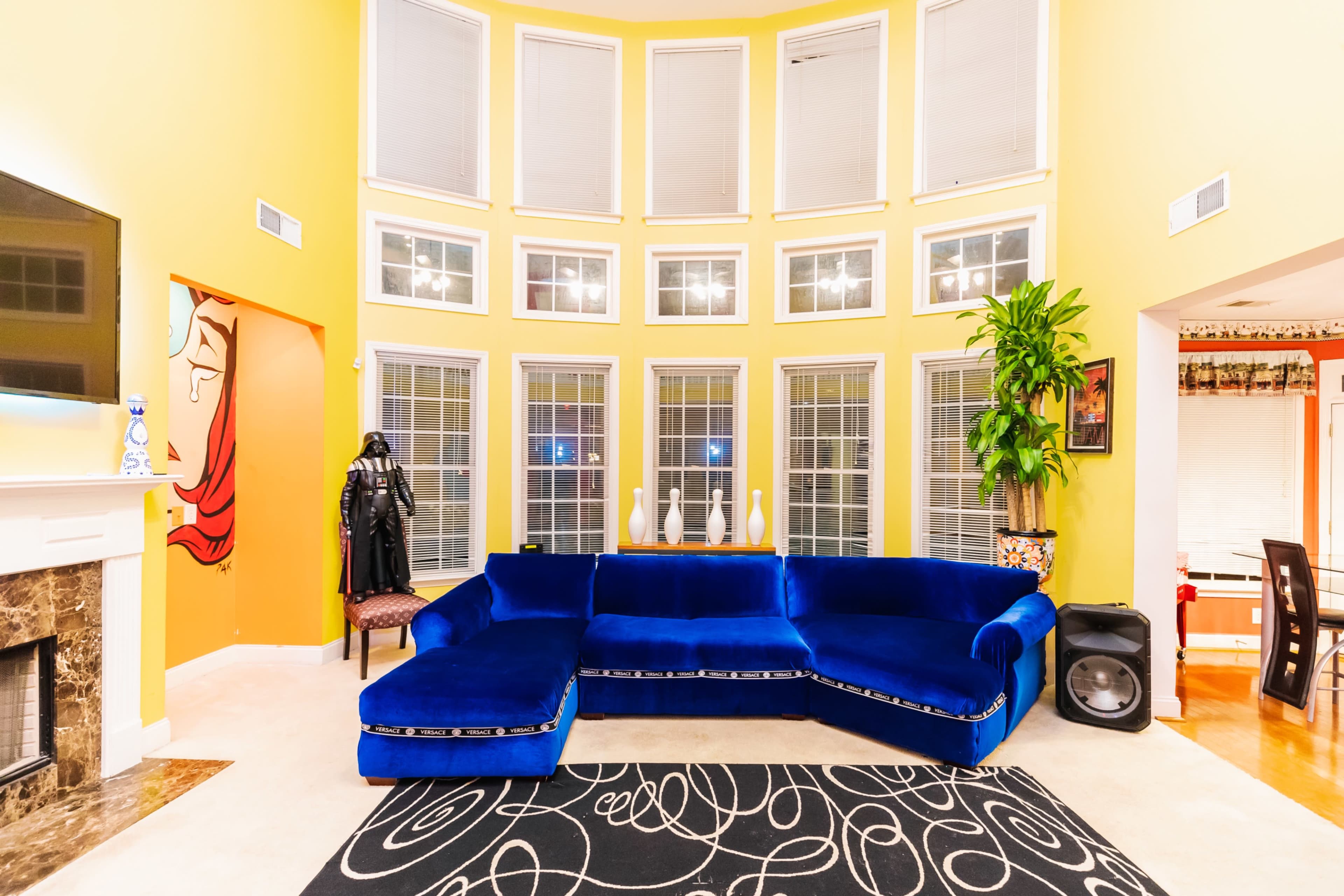 The image shows a modern living room with a blue sectional sofa, large windows, and a patterned area rug.