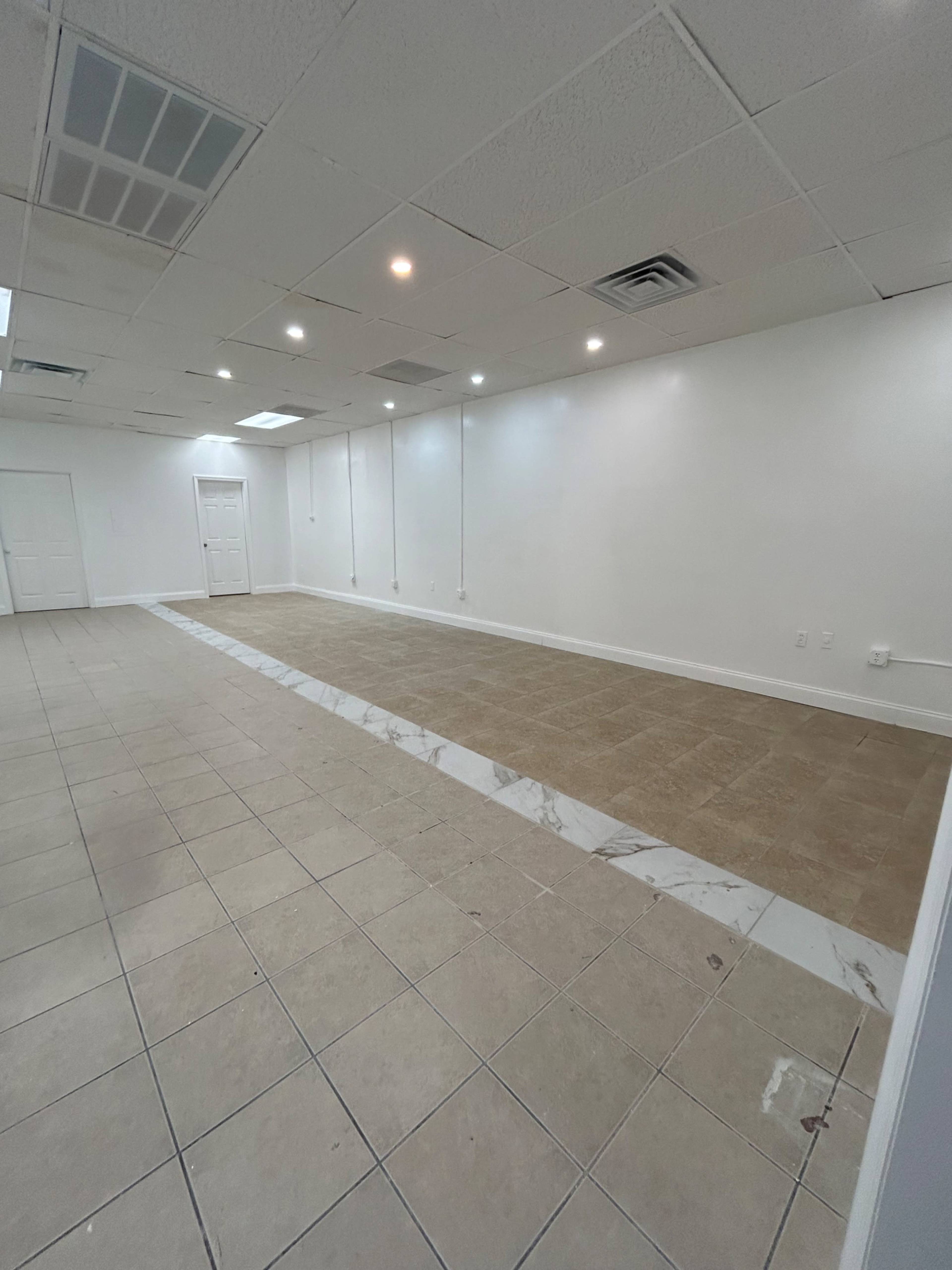 The image shows an empty commercial space with tiled flooring, featuring two different tile designs and white walls.