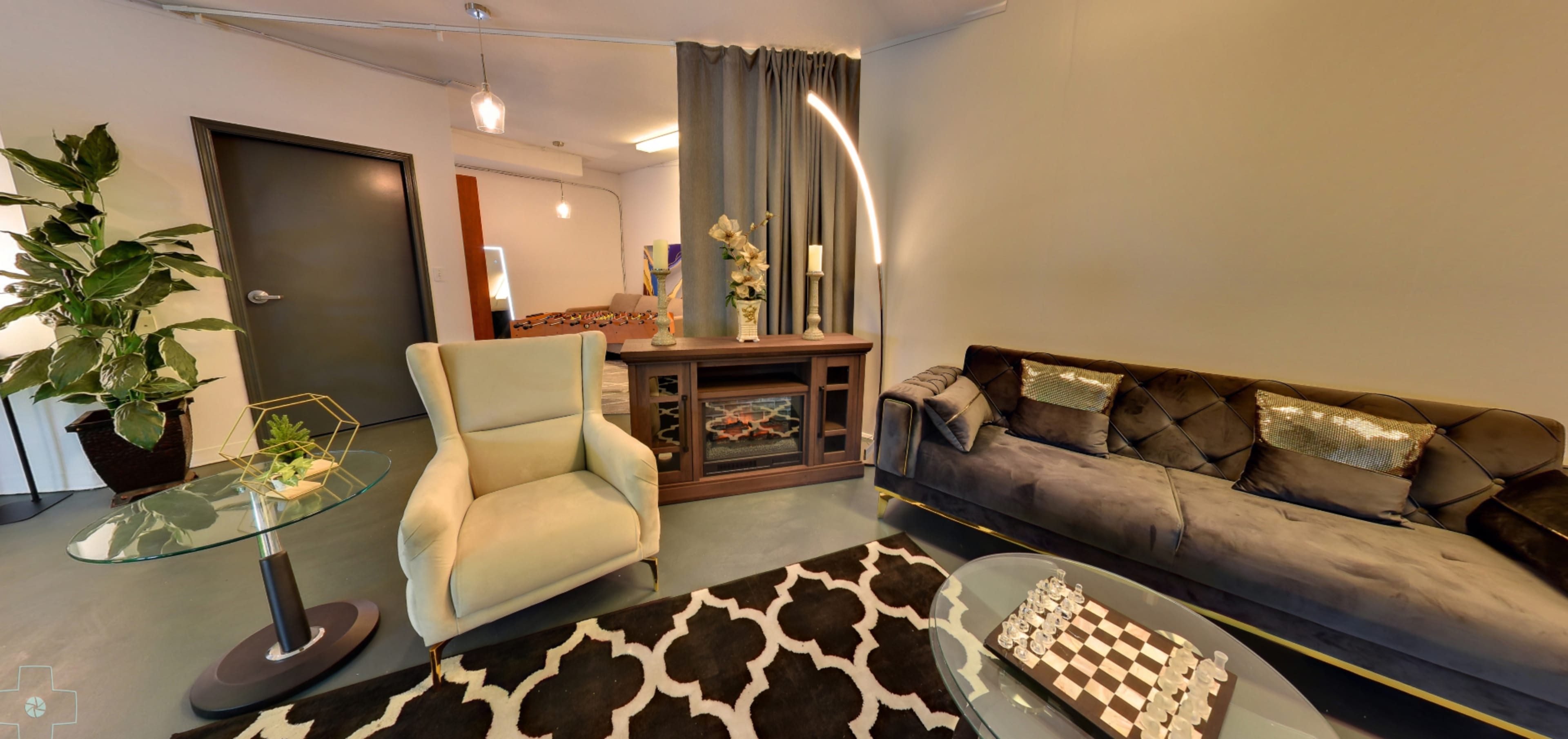 A modern living space featuring a green accent chair, a gray sofa, a glass coffee table, and a patterned rug, with a plant and decorative elements on display.