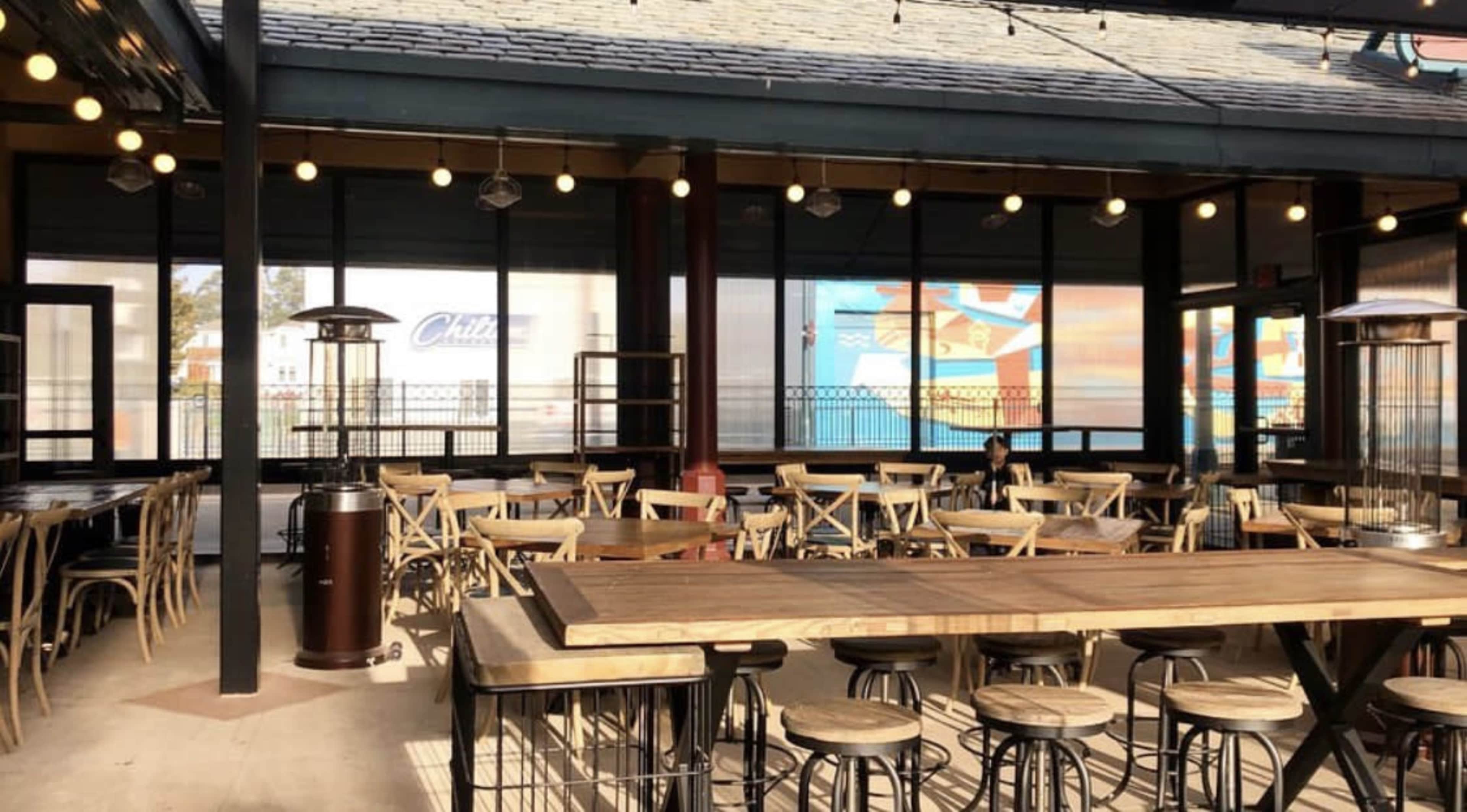 A spacious outdoor dining area with wooden tables and chairs, illuminated by string lights.
