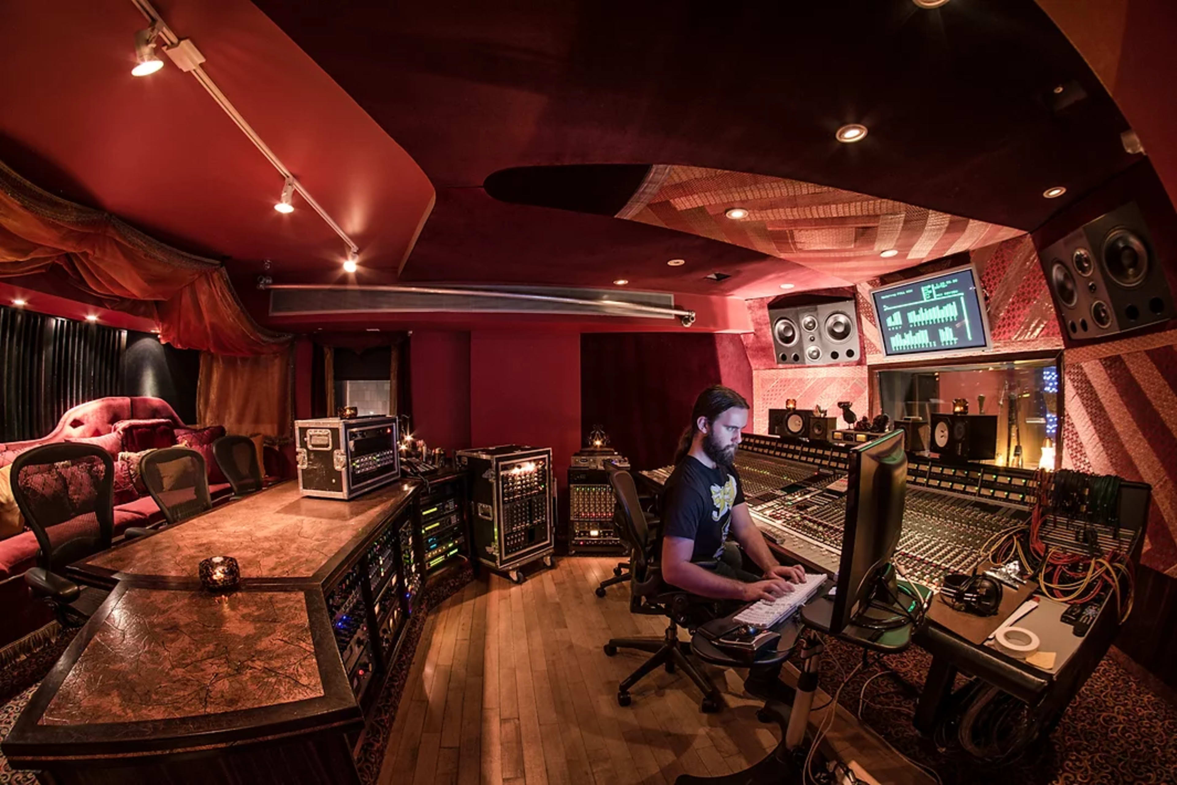 A music producer works at a large audio mixing console in a dimly lit recording studio.