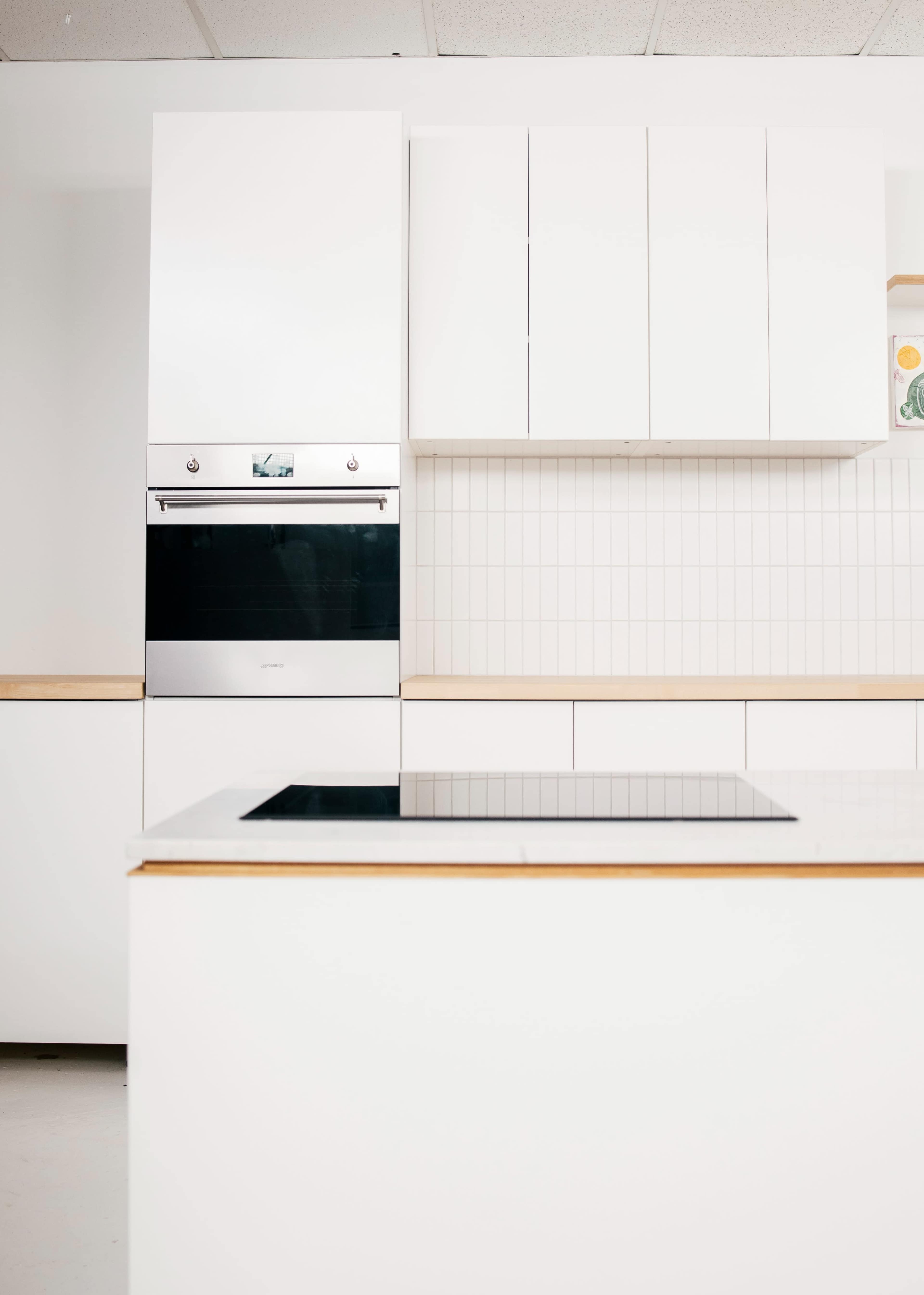A minimalist kitchen with white cabinets, a built-in oven, and a stovetop on the kitchen island.