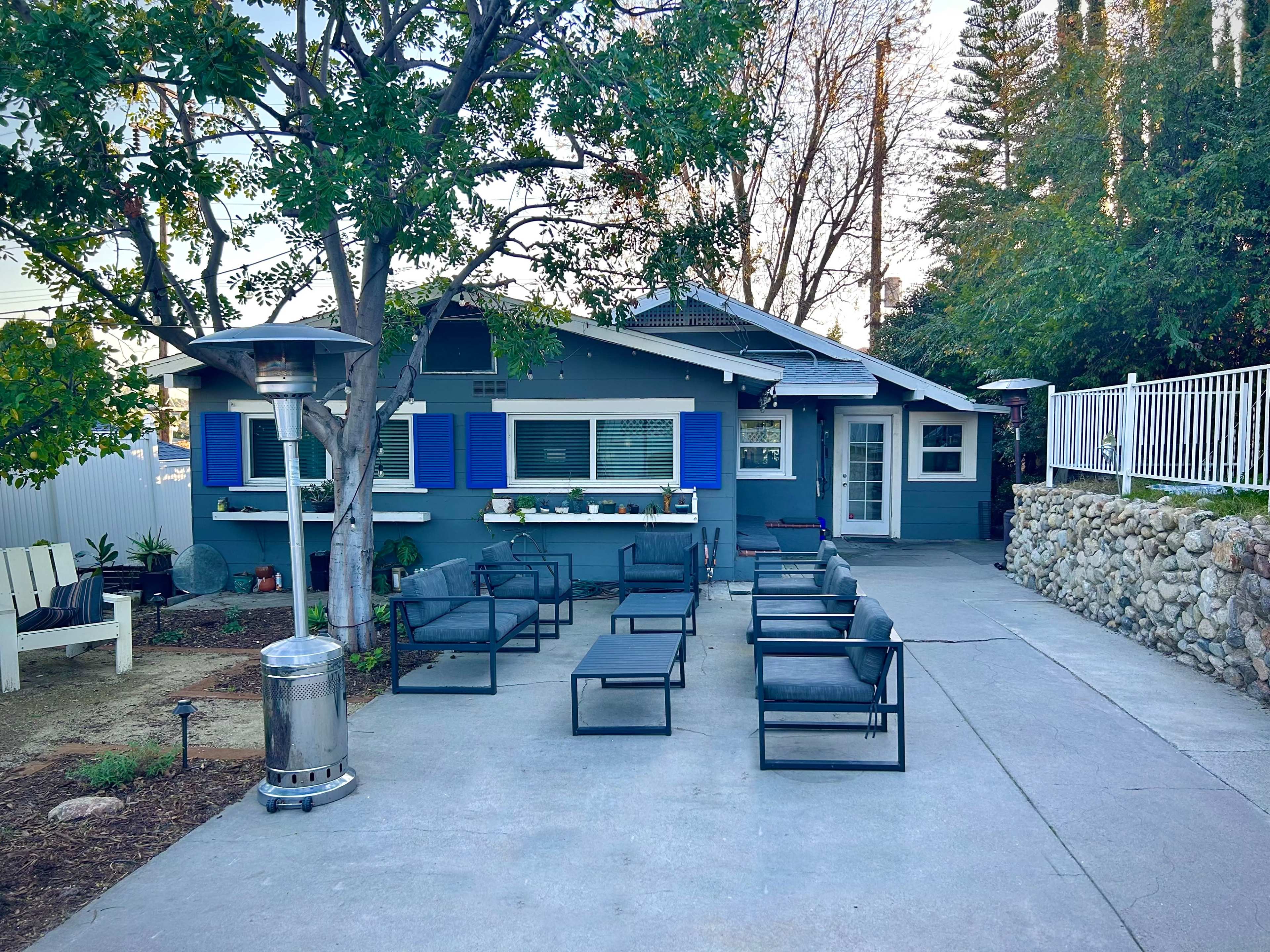 A blue-trimmed house with a patio area is surrounded by seating and landscaping features.