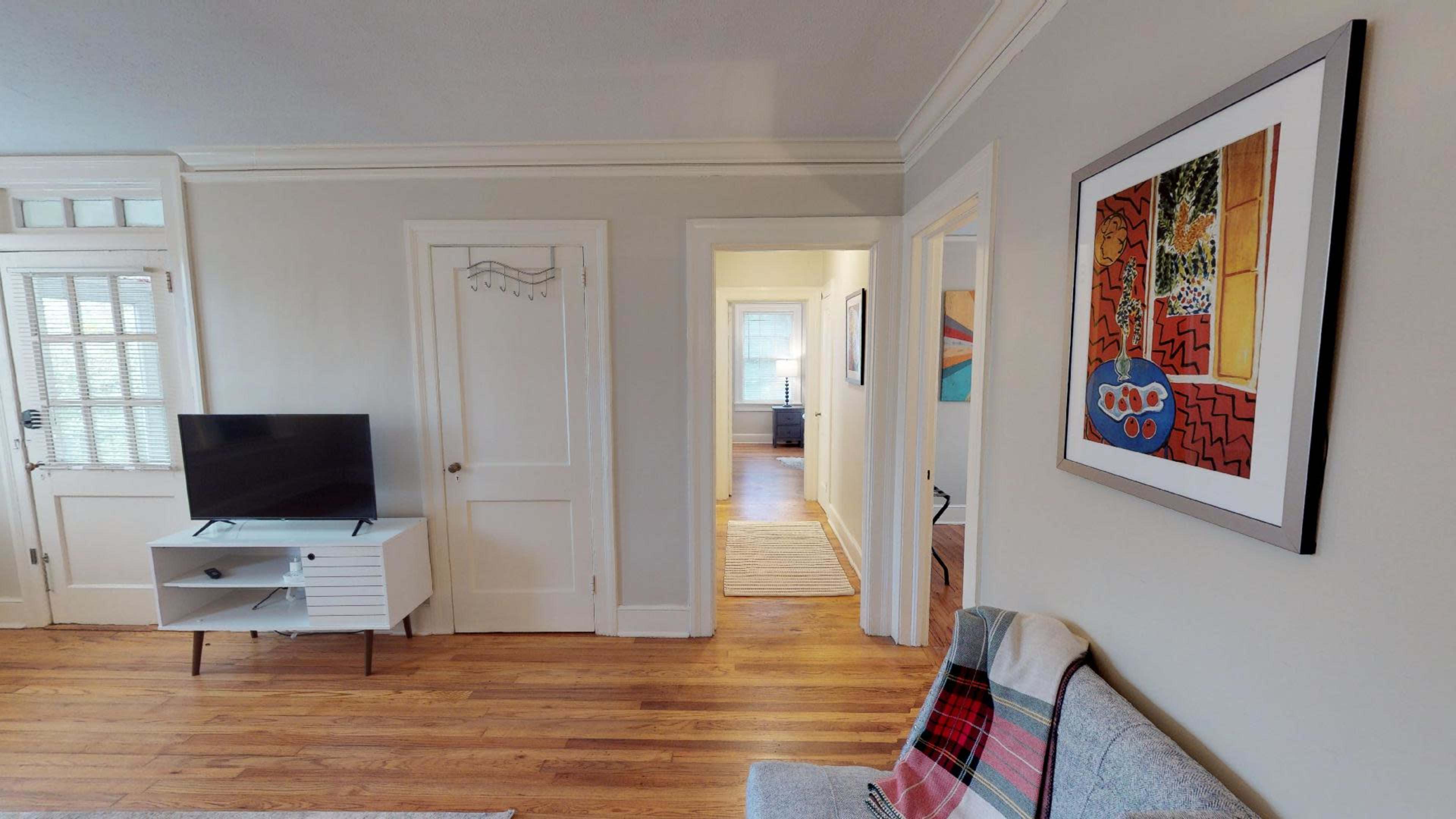 The image shows a living area with a television on a stand, a framed piece of artwork on the wall, and doorways leading to other rooms.