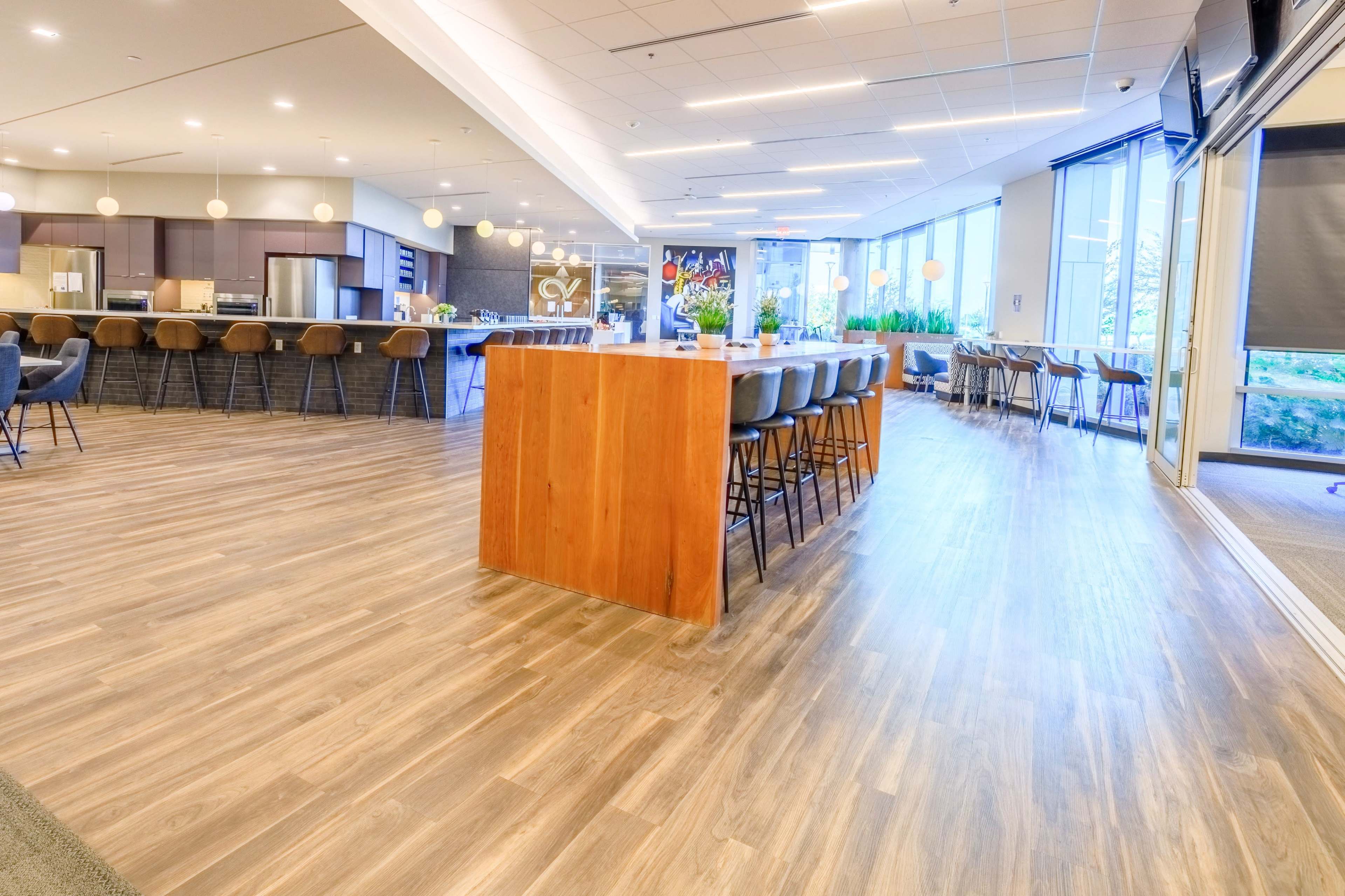 The image shows a spacious interior of a modern kitchen and dining area with wooden flooring, a central bar counter, and ample seating.