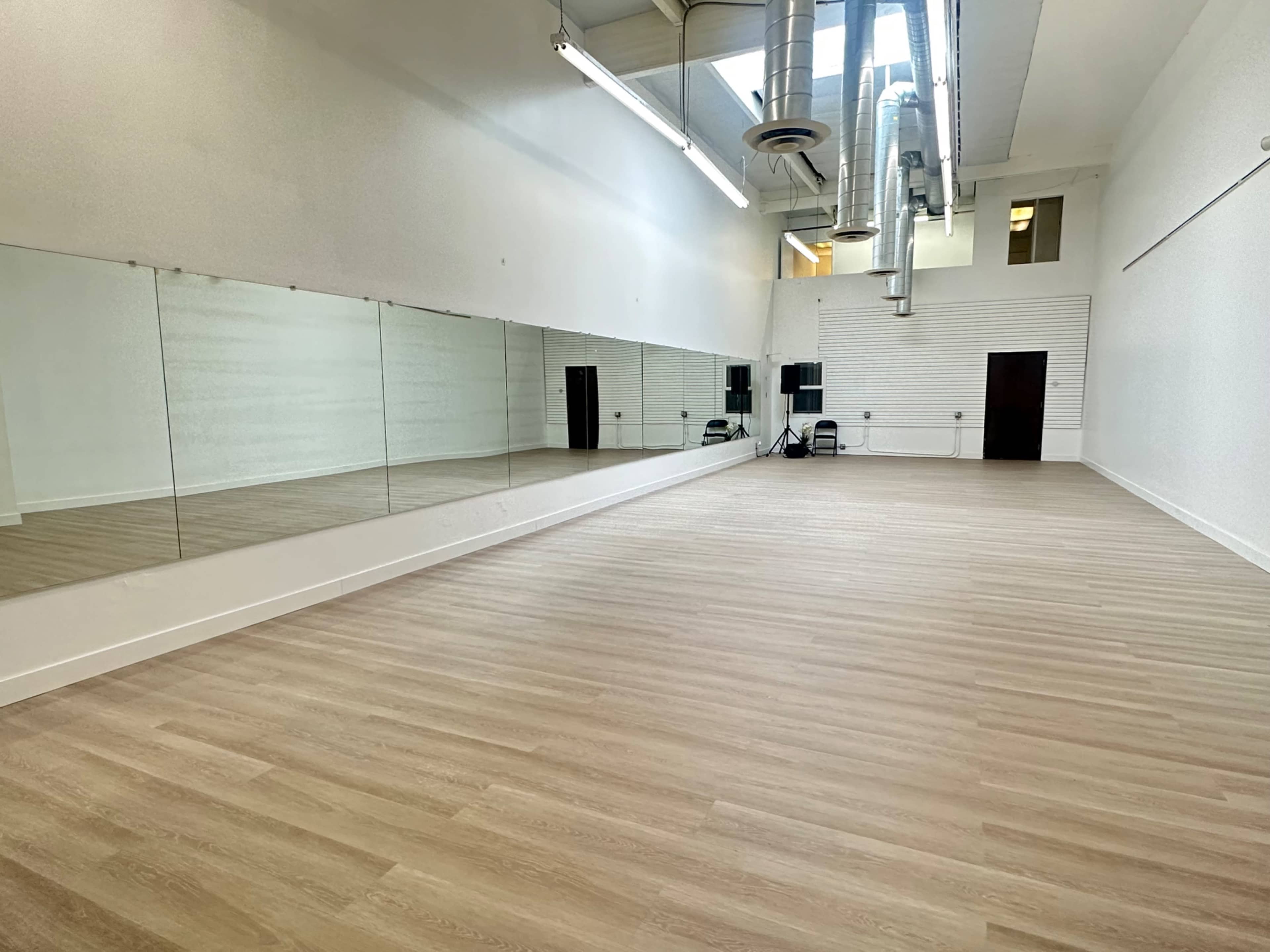 The image shows a spacious, empty dance studio with mirrored walls and wooden flooring.
