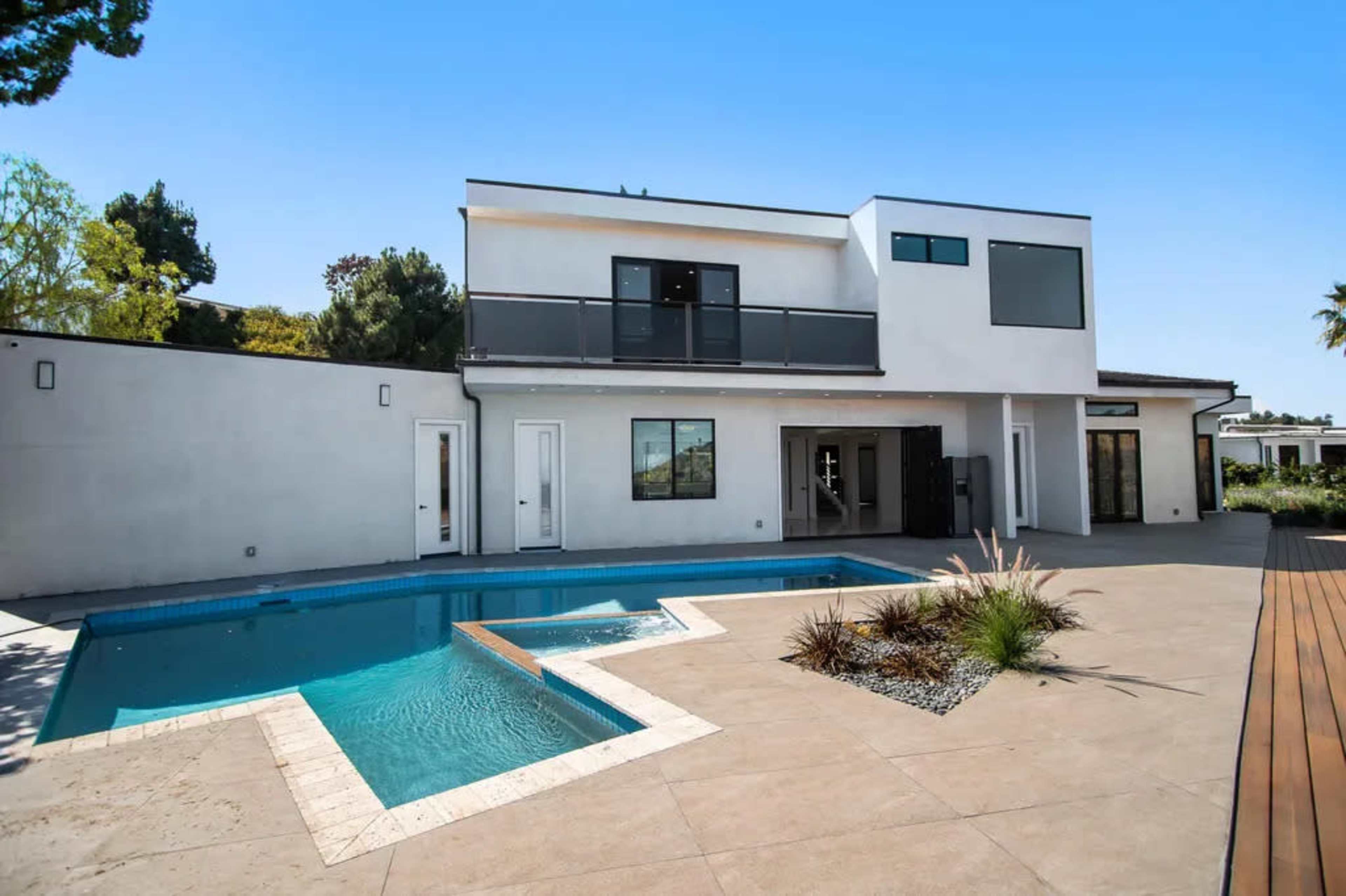 The image shows a modern two-story house with a balcony, a swimming pool, and a landscaped patio area.