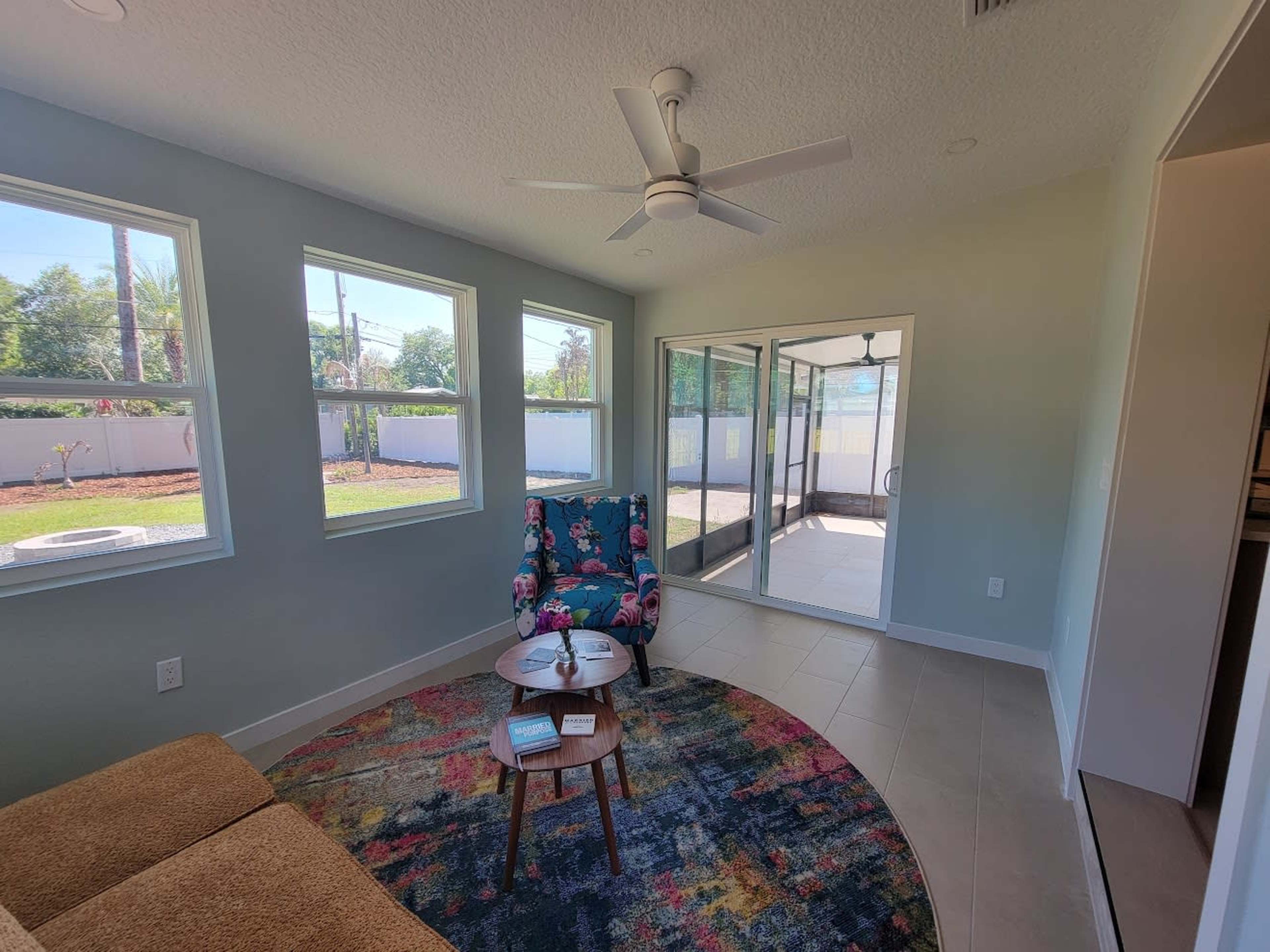 A cozy sunroom features a colorful armchair and a round table, with large windows allowing natural light to fill the space.