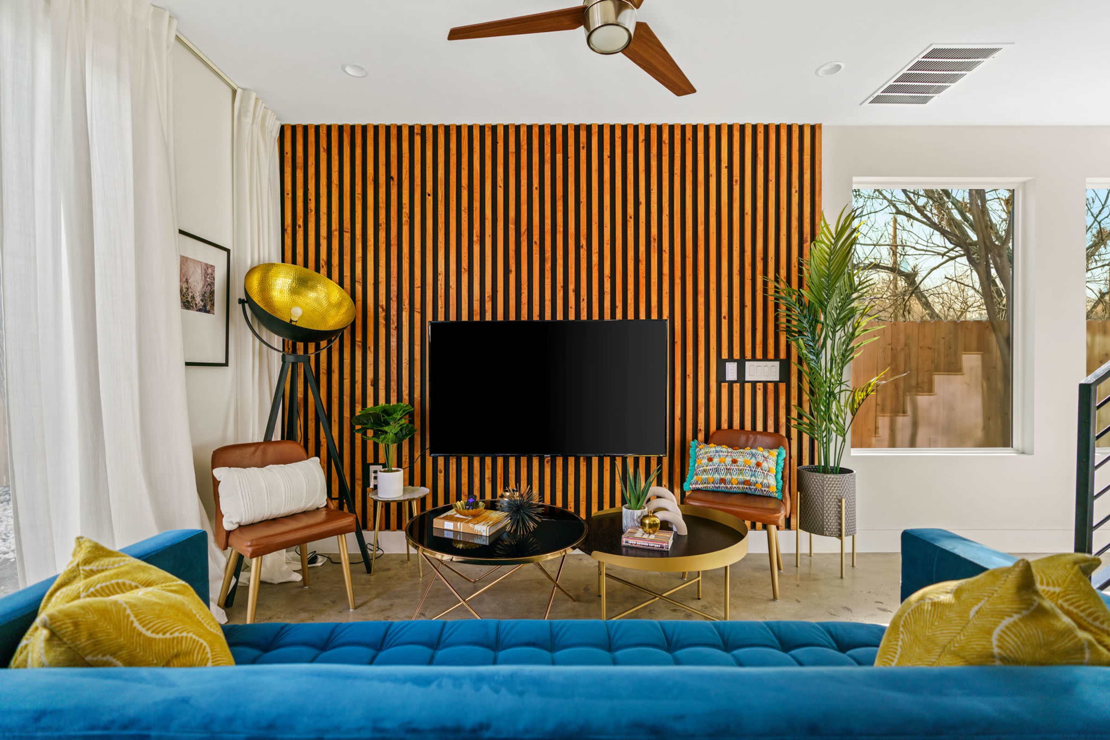 A modern living room features a textured wood accent wall, a large television, and a mix of furniture including a blue sofa, a round coffee table, and a floor lamp.
