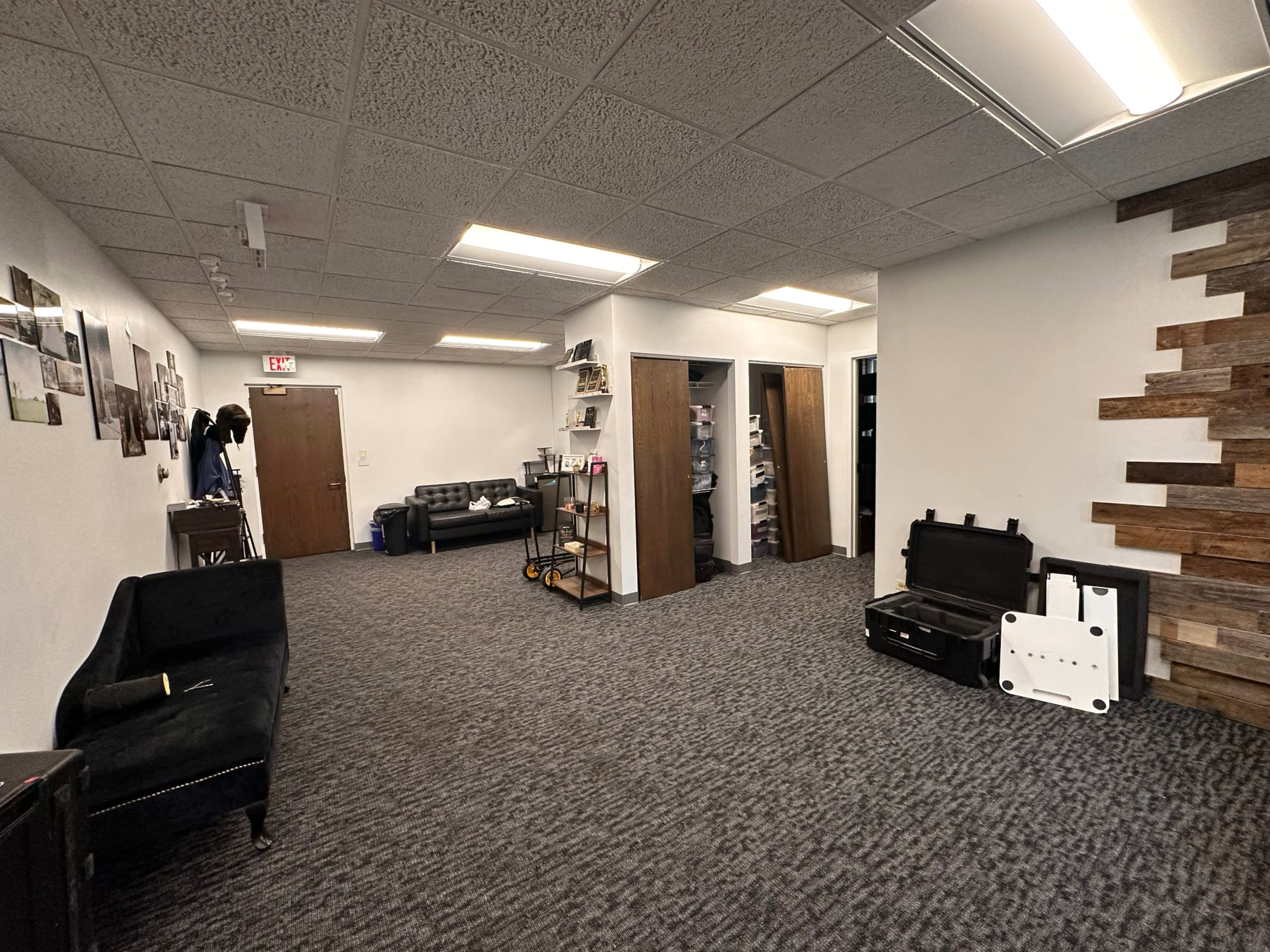 The interior of a spacious office or meeting room features textured carpeting, a black sofa, two tall wooden cabinets, and photos displayed on the walls.
