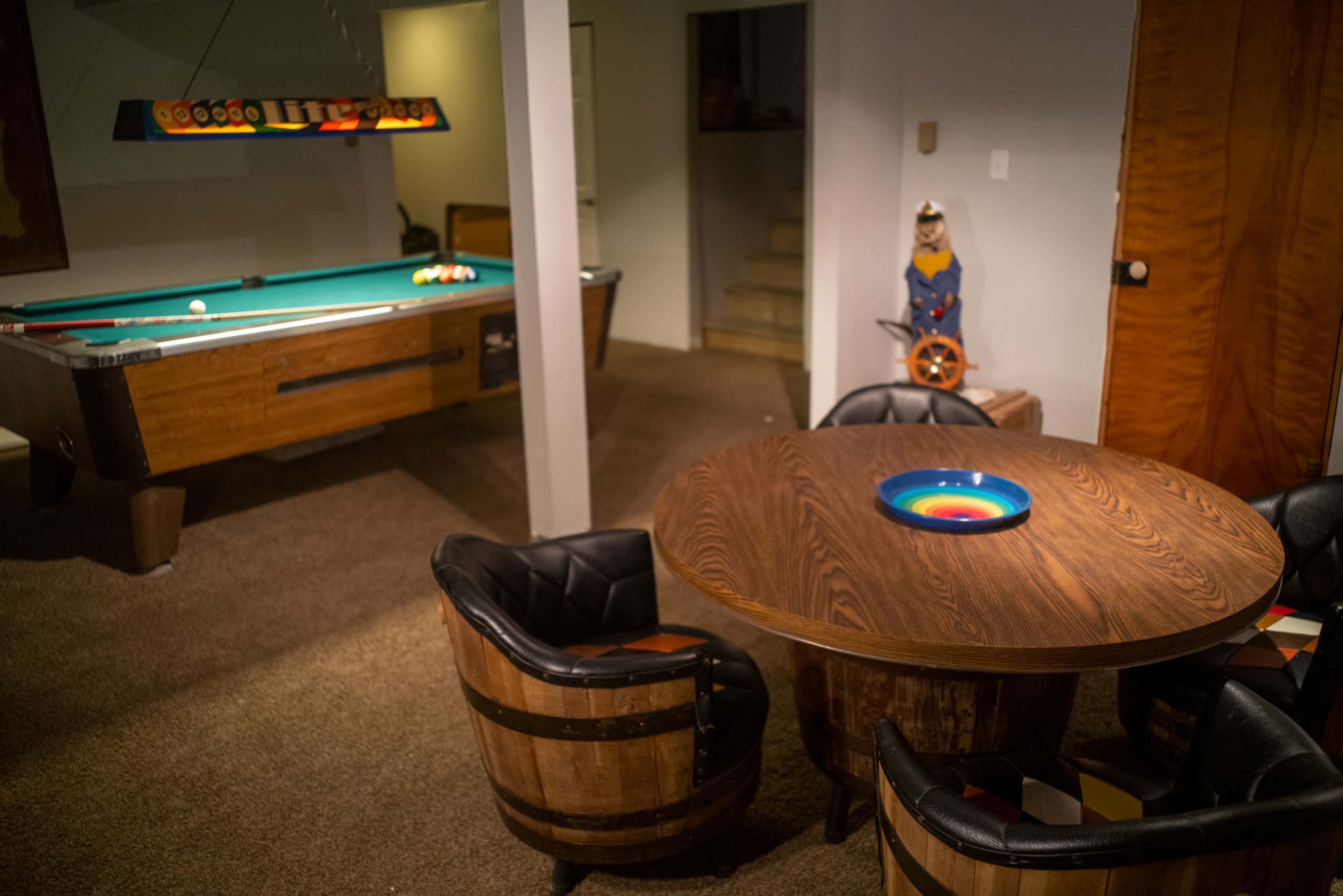 A basement game room featuring a pool table and a circular wooden dining table surrounded by barrel-shaped chairs.