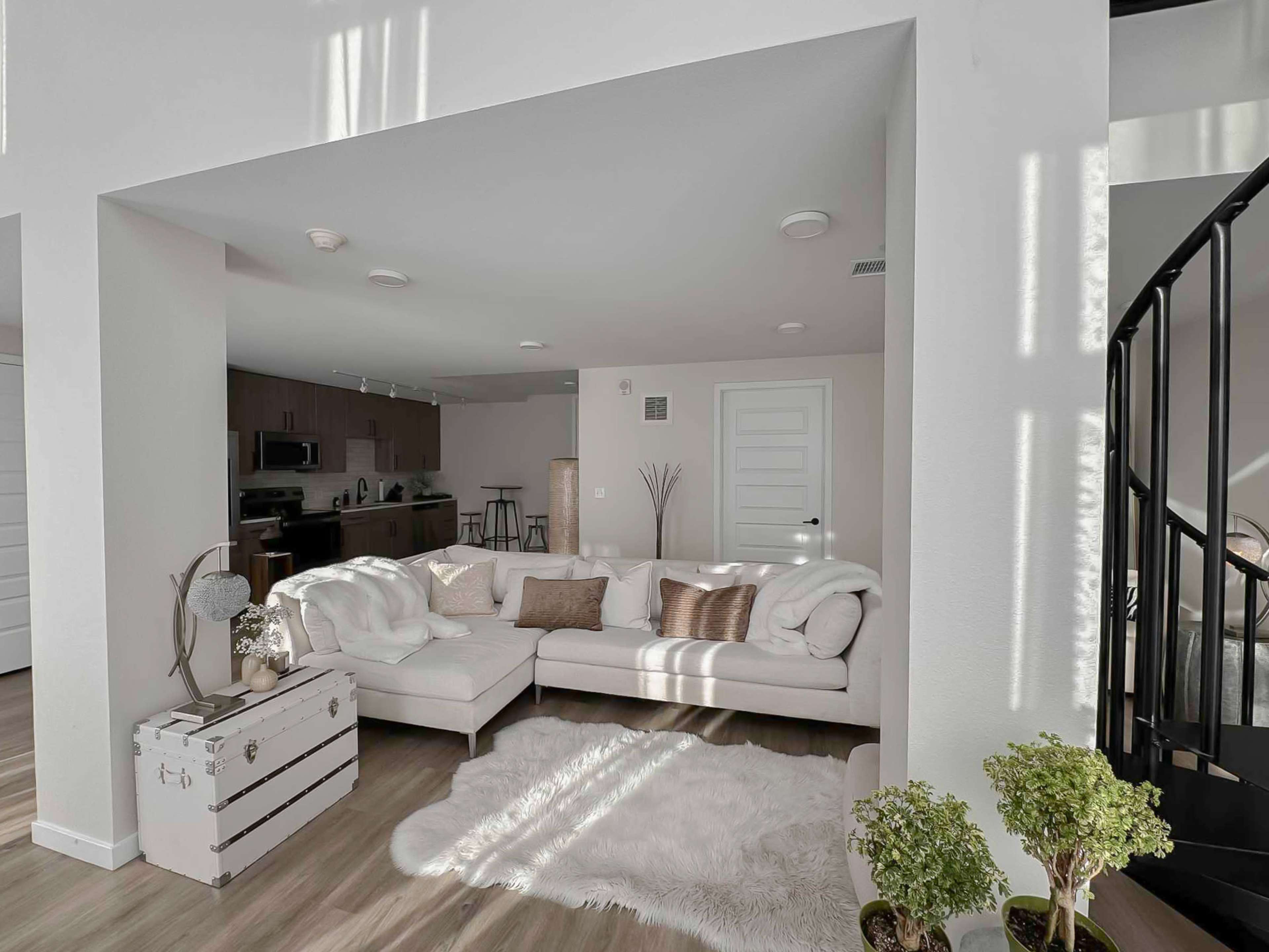 The image depicts a modern living room with a white sectional sofa, a decorative trunk, and natural light streaming through the space.