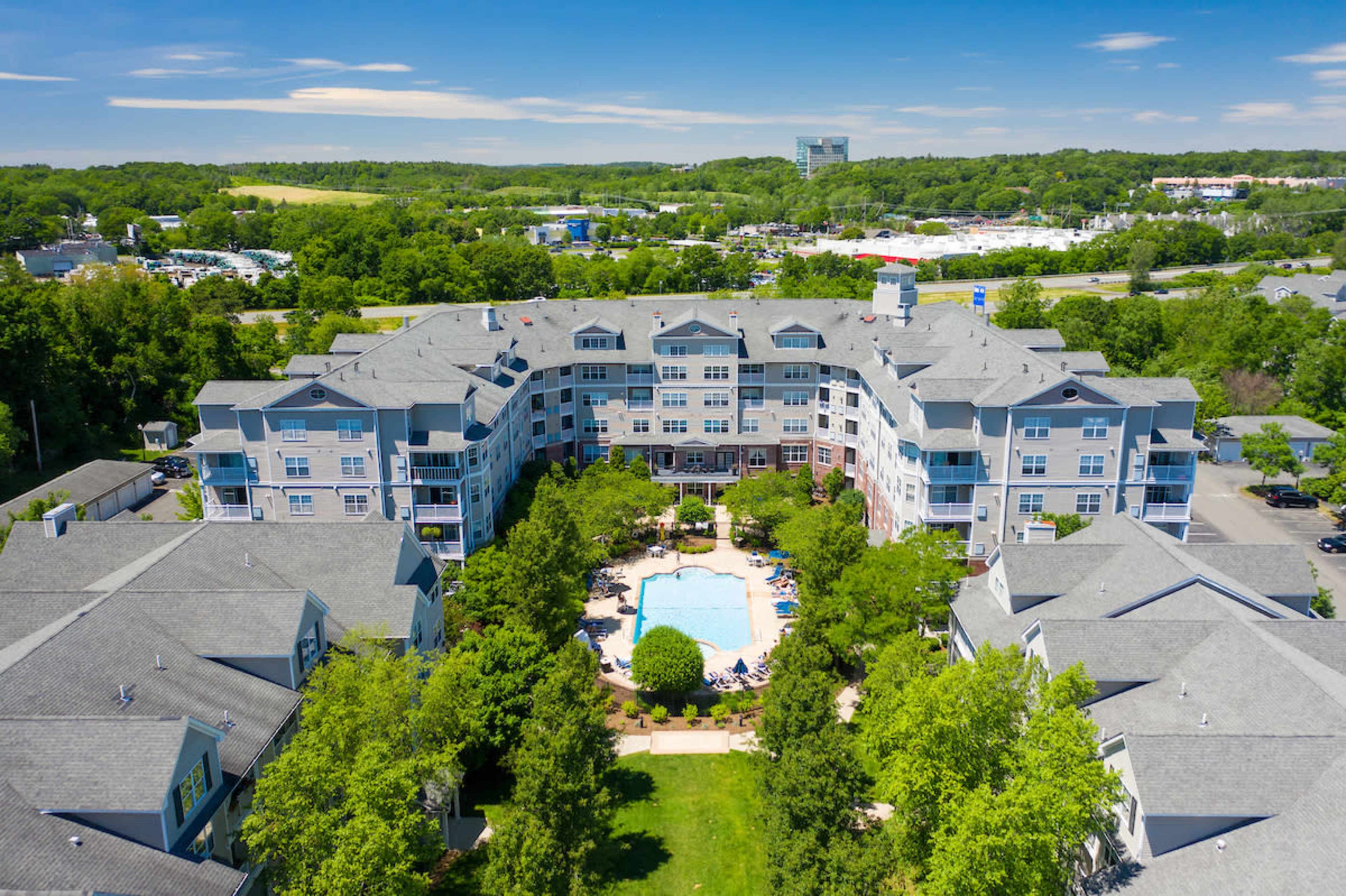 An aerial view of a residential complex with a central pool surrounded by buildings and greenery.