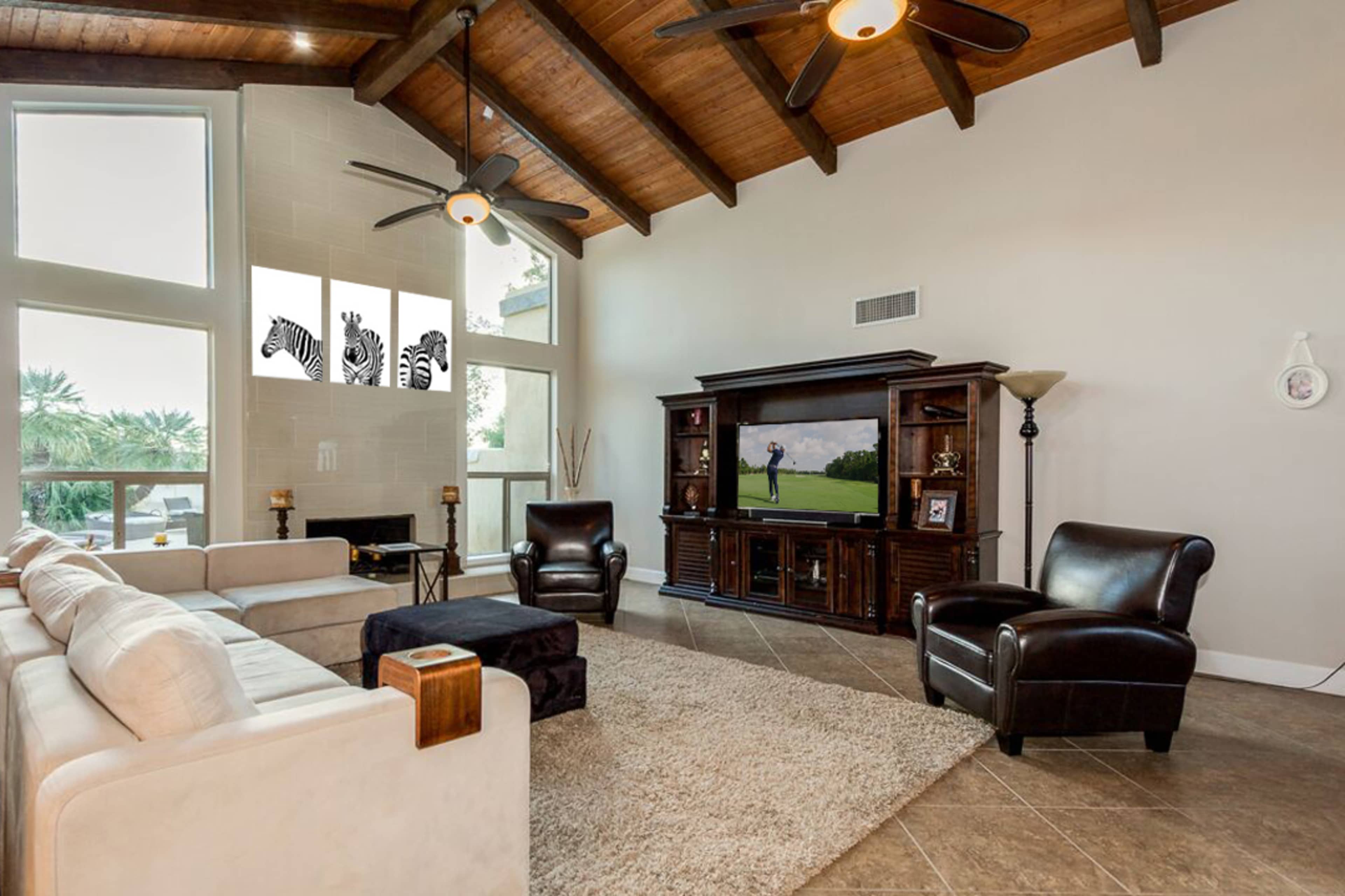 A spacious living room with a large flat-screen TV, comfortable seating arrangements, and high wooden ceilings.