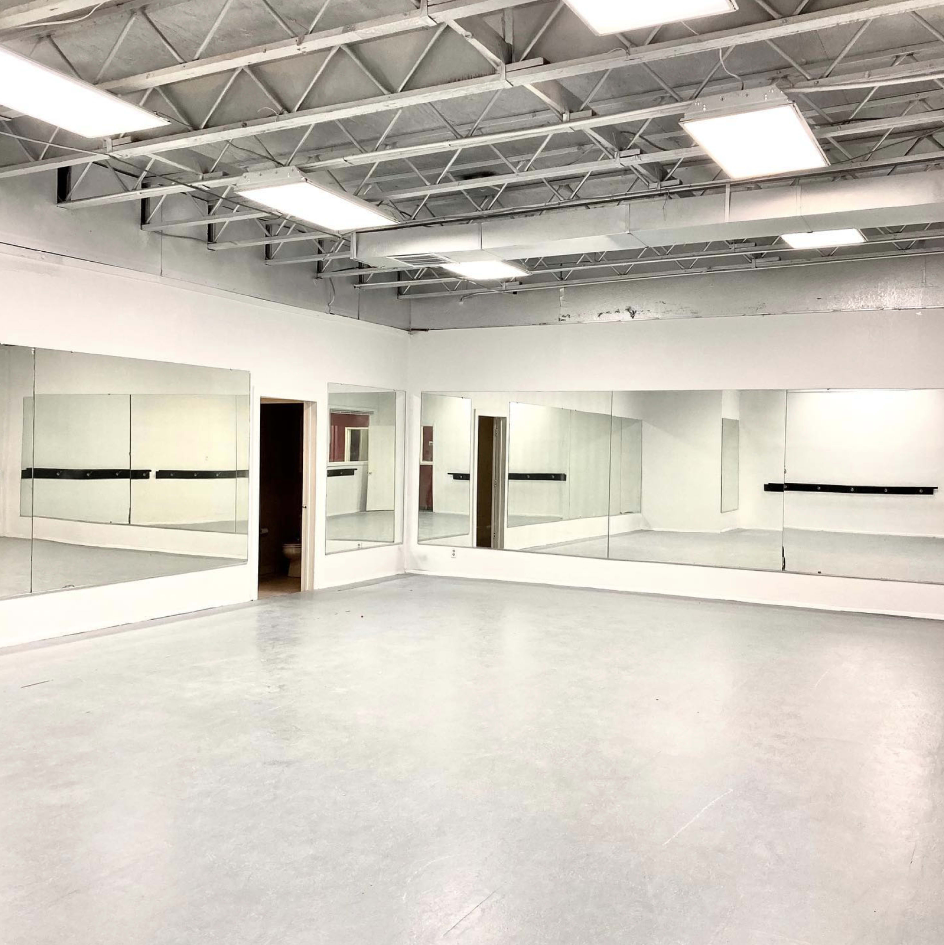 A spacious dance studio with mirrored walls and a gray floor under bright overhead lights.