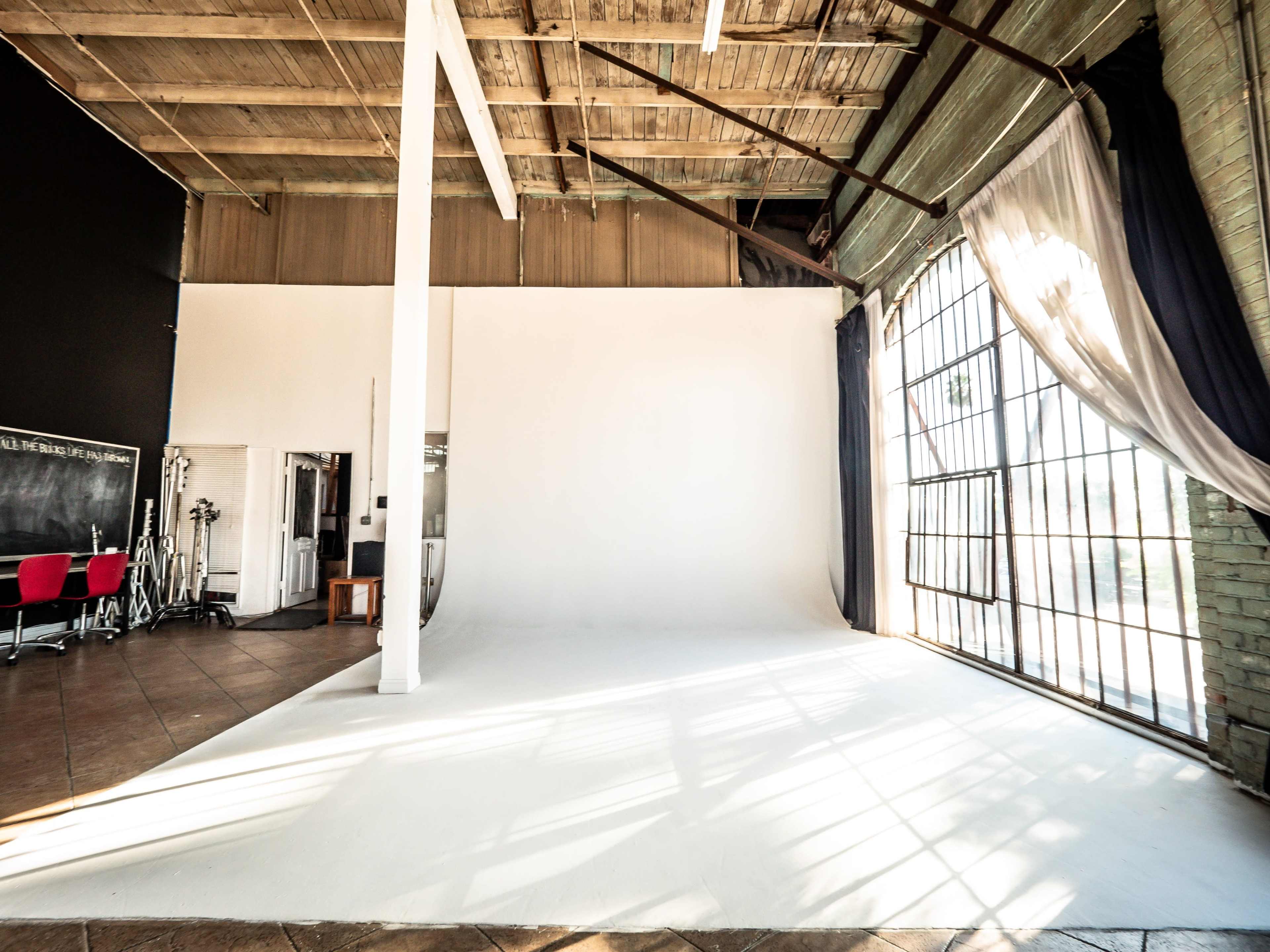 A spacious photography studio with a white backdrop, large windows, and exposed wooden beams.
