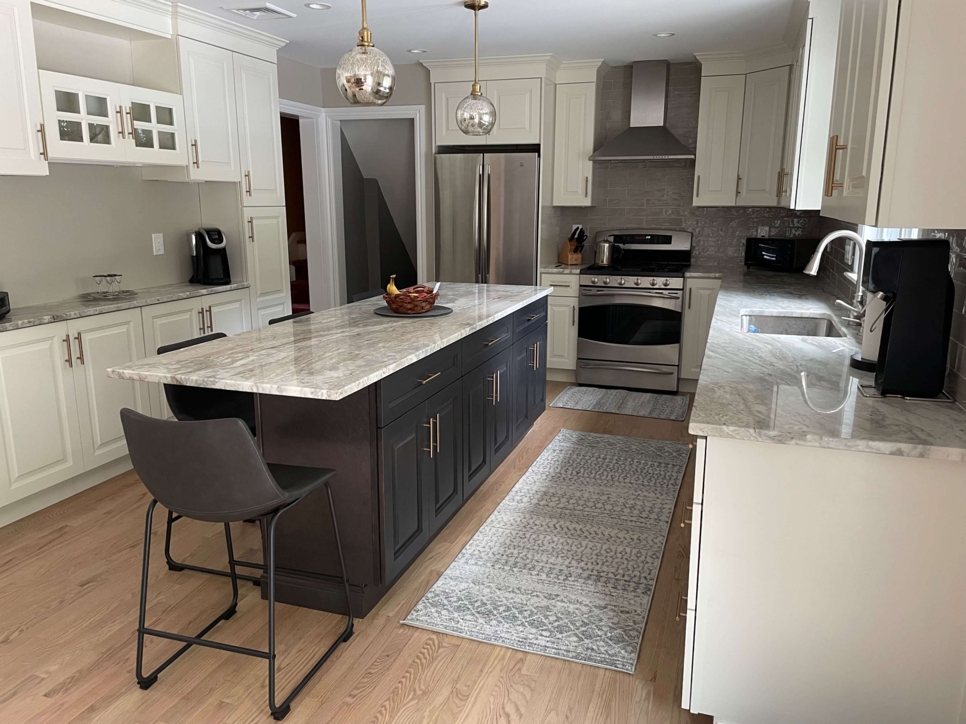 A modern kitchen featuring a central island with a gray countertop, stainless steel appliances, and light-colored cabinets.
