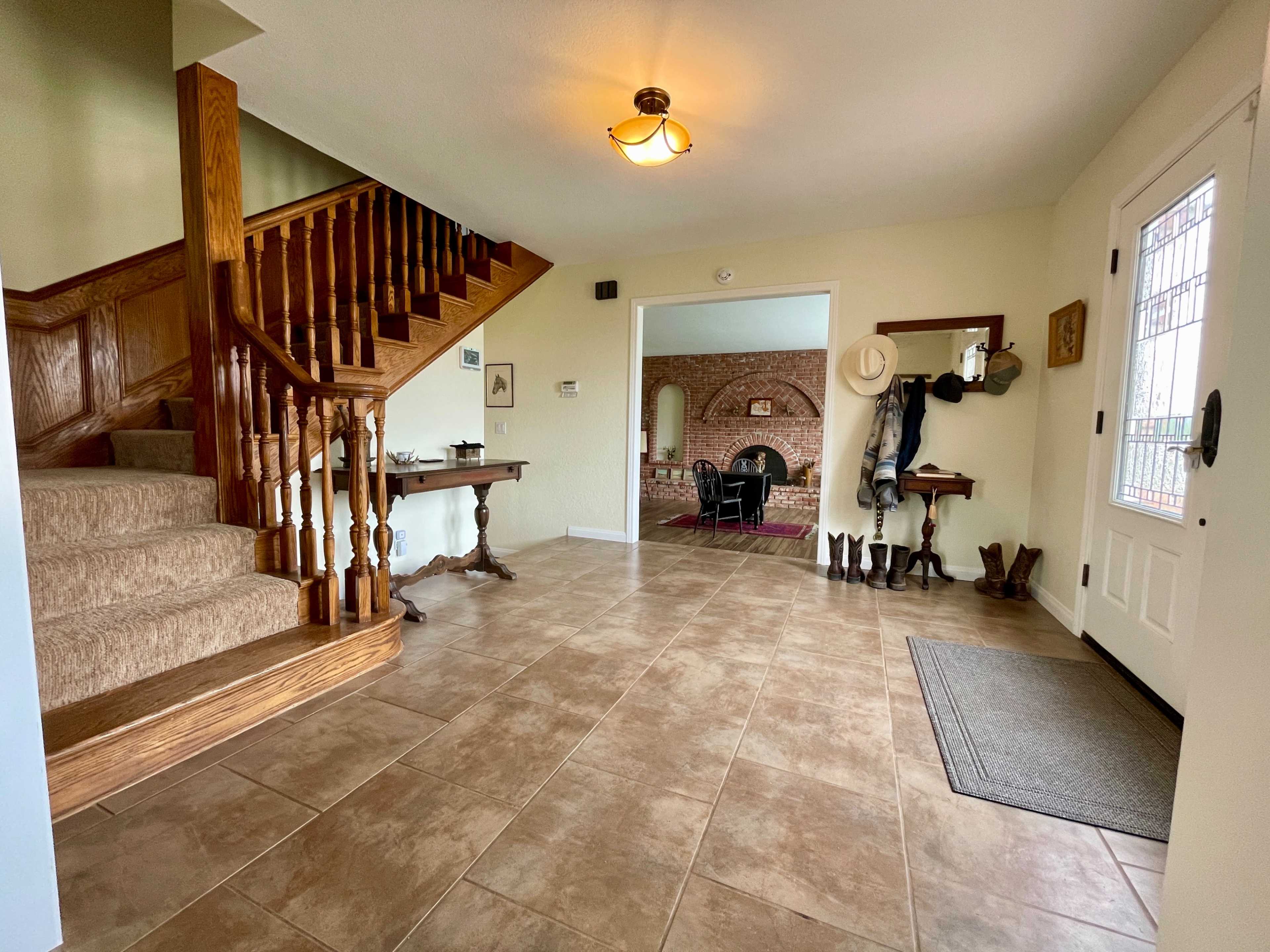 The entryway features a wooden staircase, tiled floor, and a coat rack beside the front door.