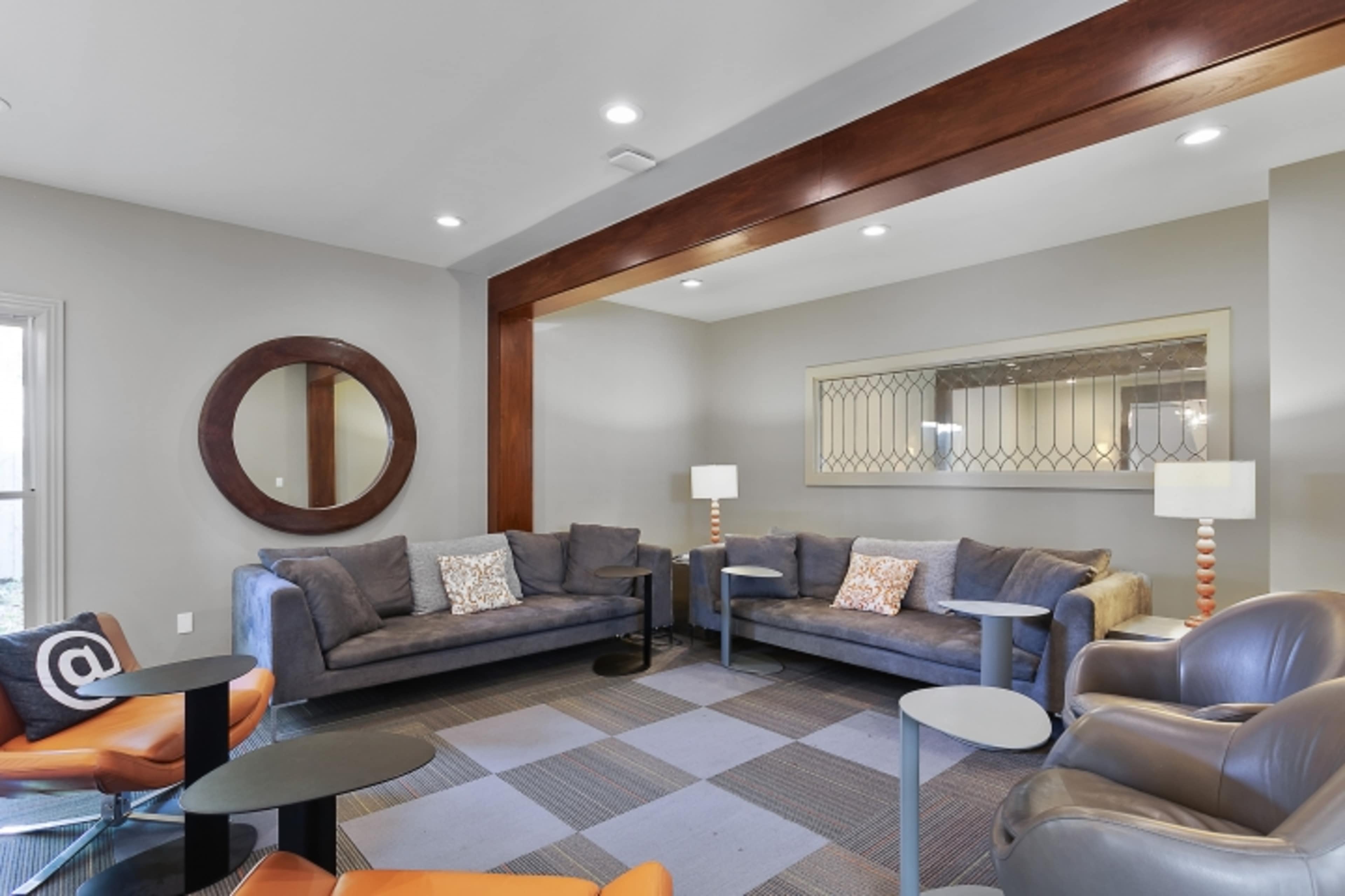 A modern lounge area with two gray sofas, several small tables, and a round mirror on the wall.