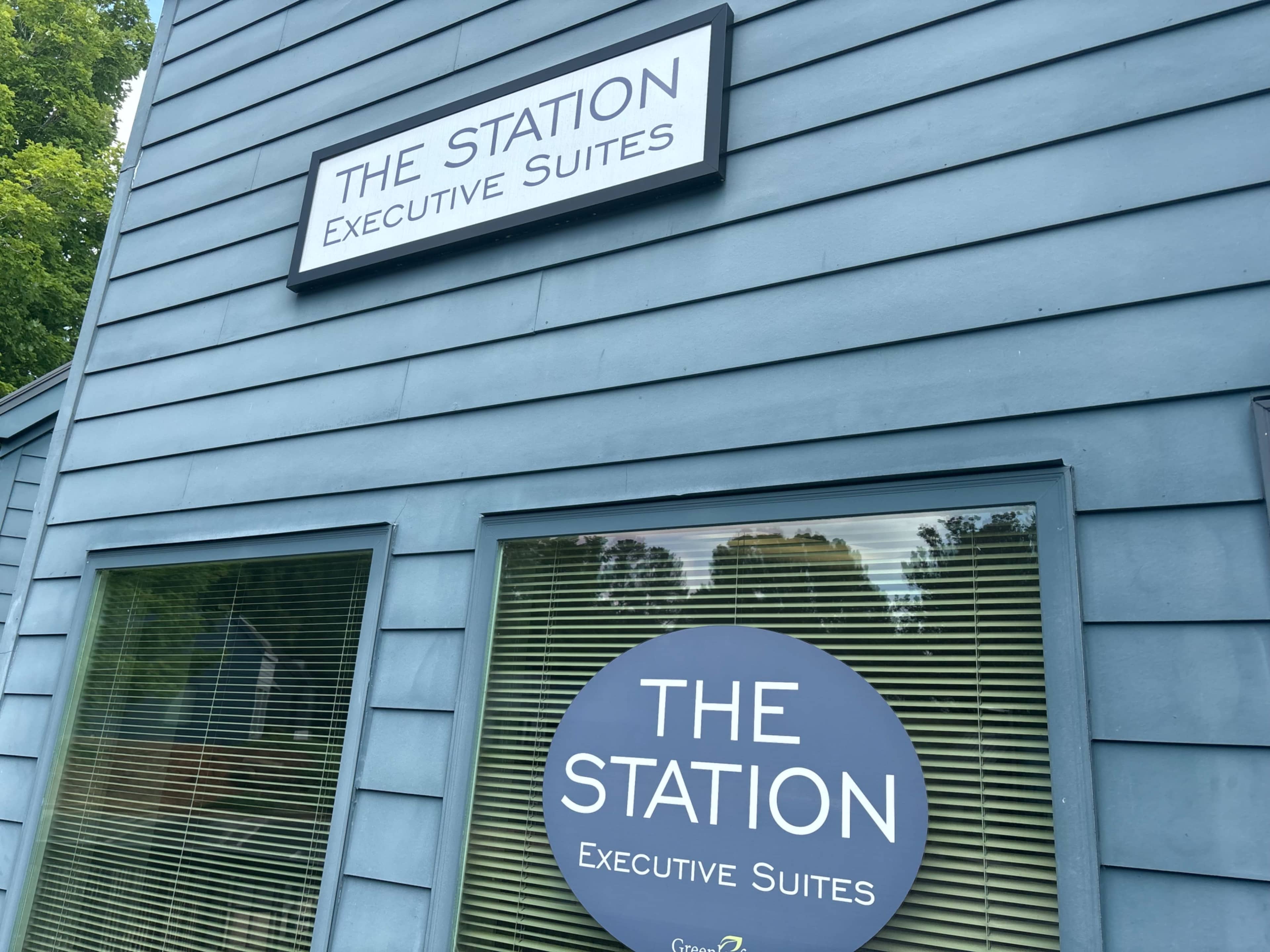 A blue building exterior with a sign that reads "THE STATION Executive Suites" above a large round window decal with the same text.