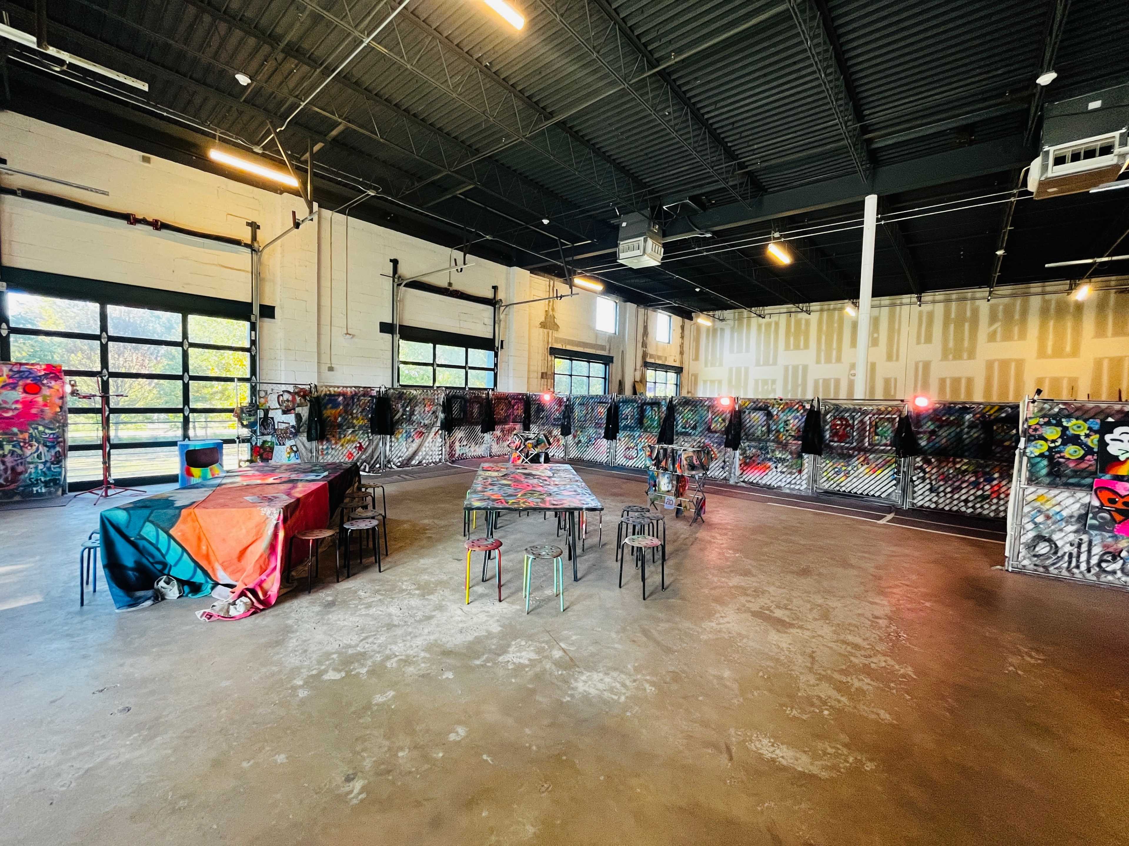 An art studio with various colorful graffiti artworks displayed on walls and tables, accompanied by metal chairs.